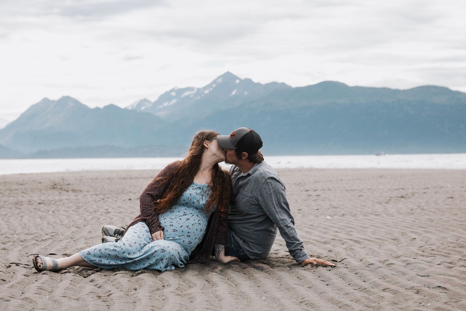 Romantic couple lying together on a rocky beach overlooking mountain views.