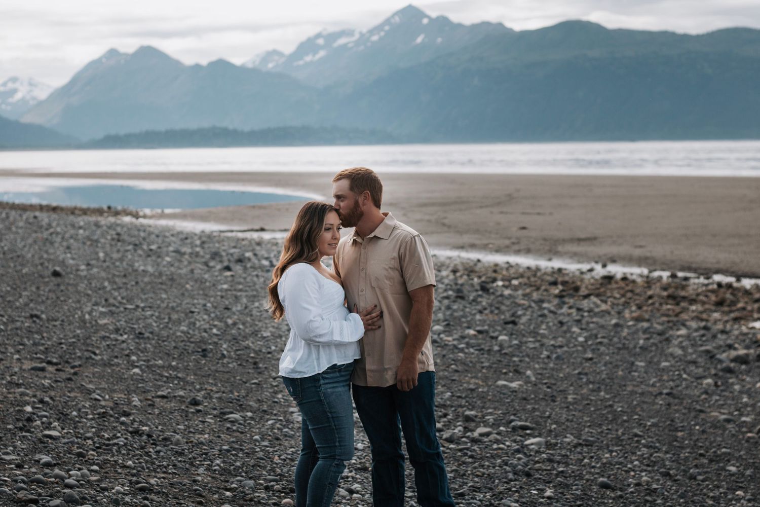 Couple enjoying playful moments on rocky beach with mountain backdrop in Alaska
