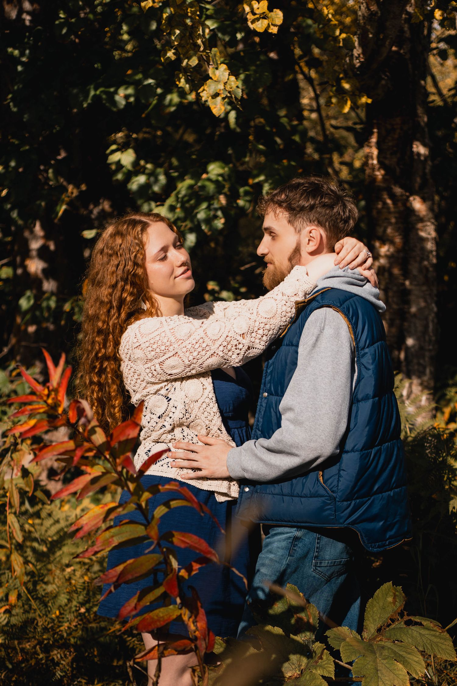 Romantic couple sharing intimate moments in a wooded area with autumn foliage.