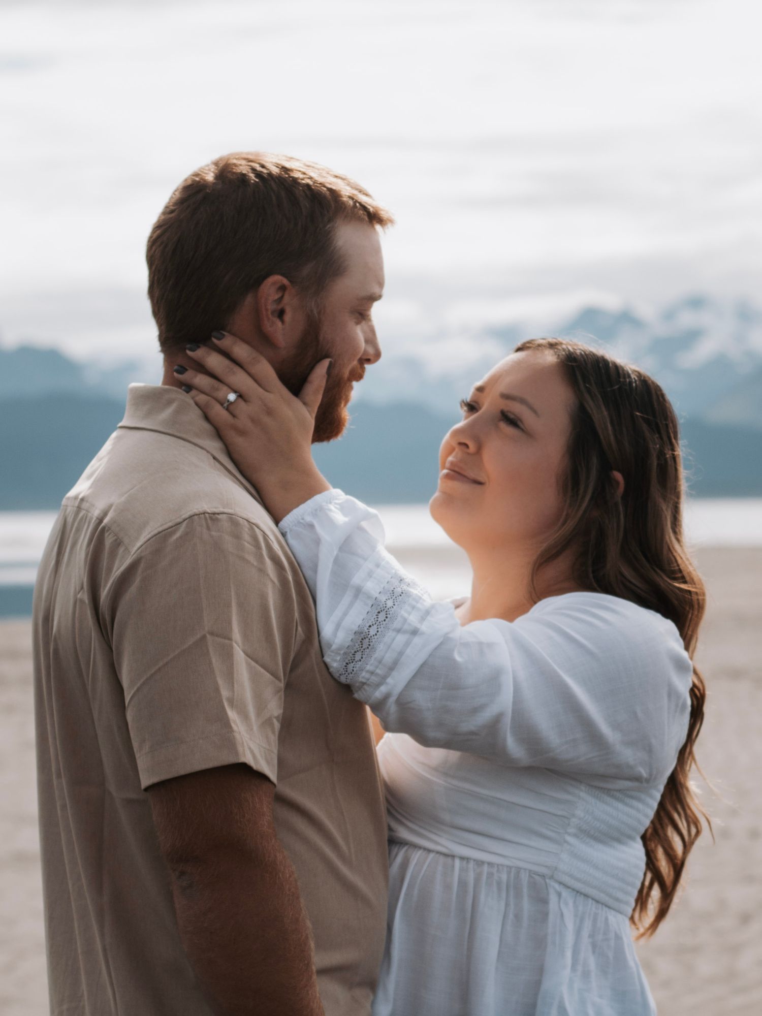 Intimate moment captured on beach with mountain backdrop and overcast sky in Alaska