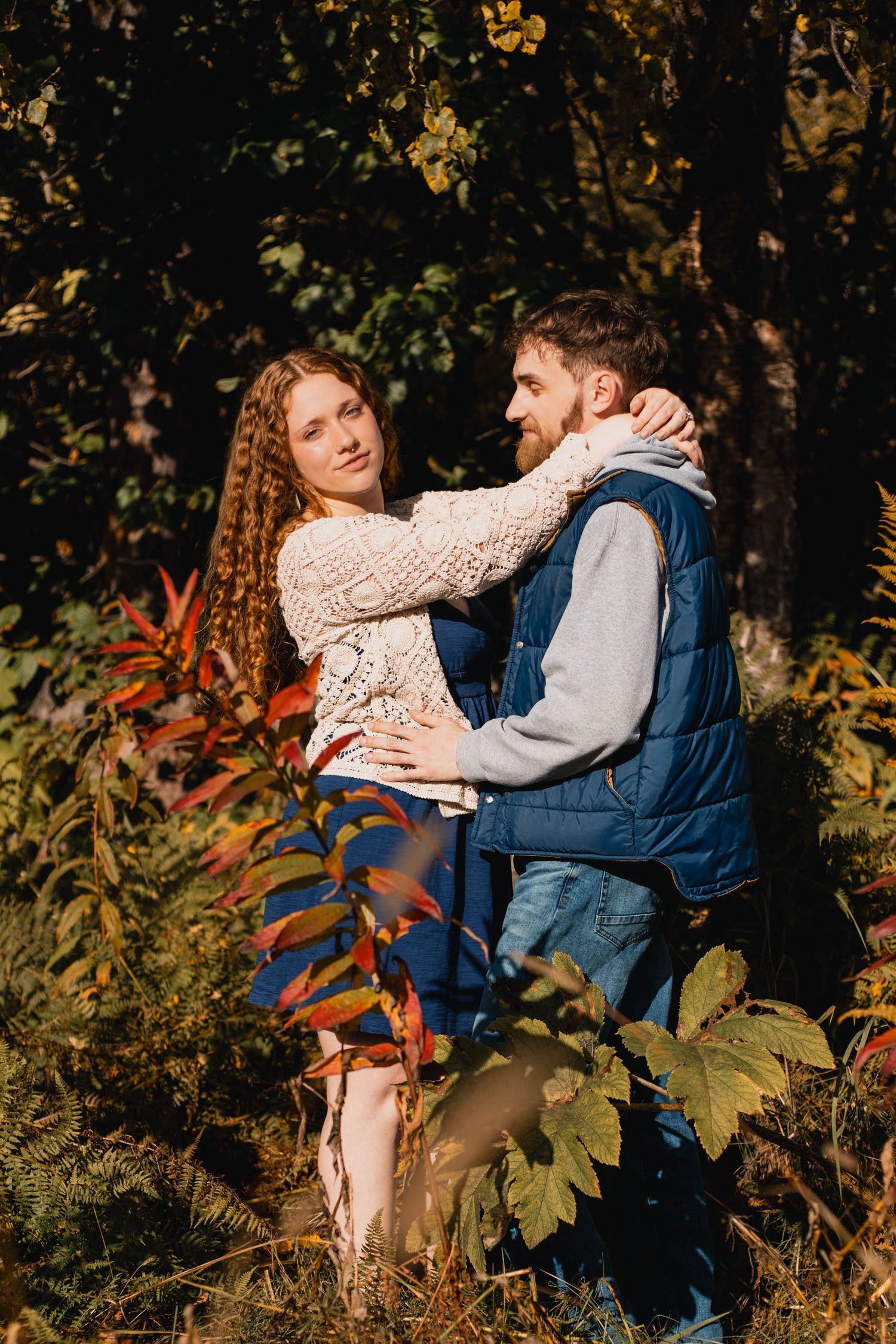 A couple shares an intimate embrace among autumn foliage in a romantic outdoor photo shoot.