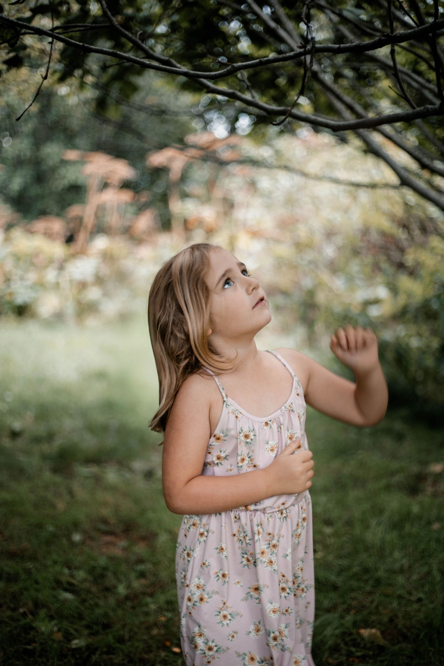 A young person in a floral dress expresses joy while dancing and twirling outdoors in a natural garden setting.