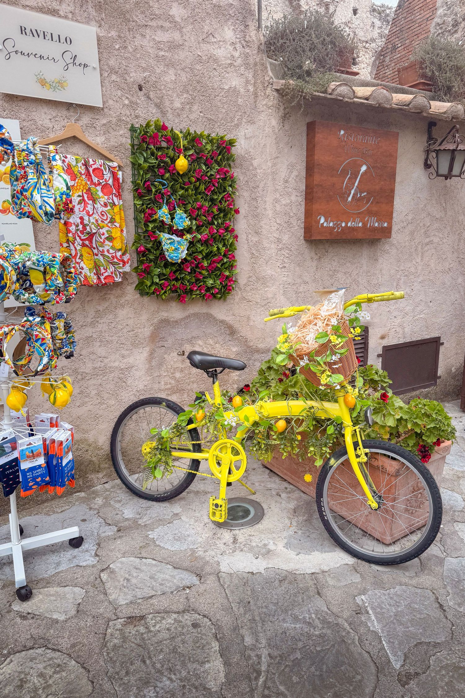 A bright yellow bicycle mounted as decorative art piece on a rustic stone wall with colorful flower arrangements.