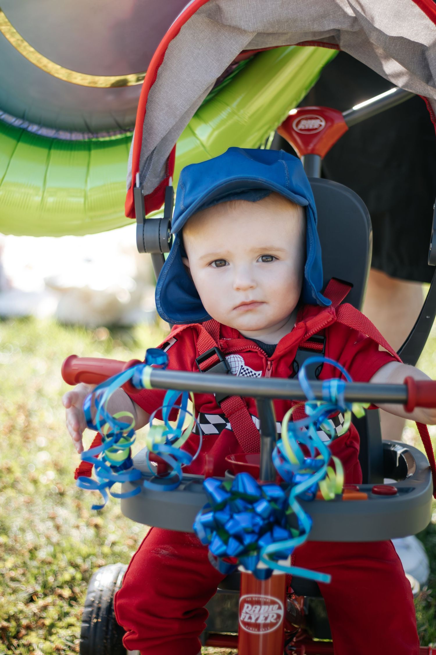 Close-up shots of baby in red outfit and blue cap sitting in decorated stroller.