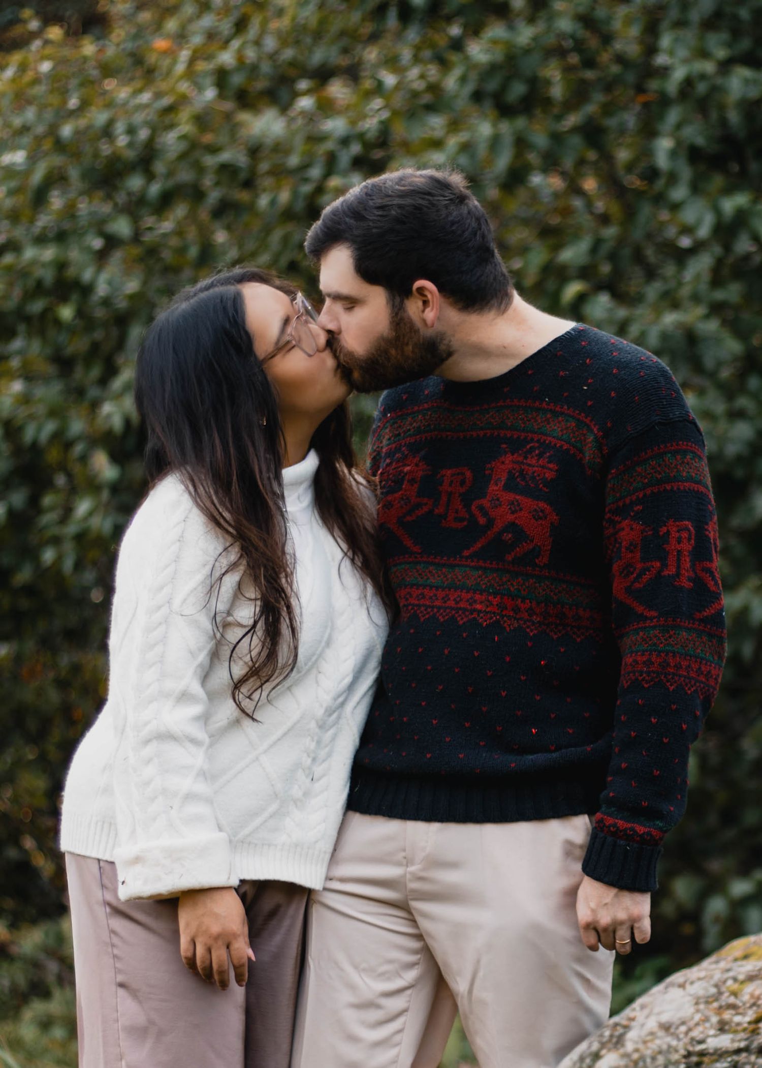 A couple in contrasting white and black sweaters share tender moments in a series of outdoor photos against foliage.