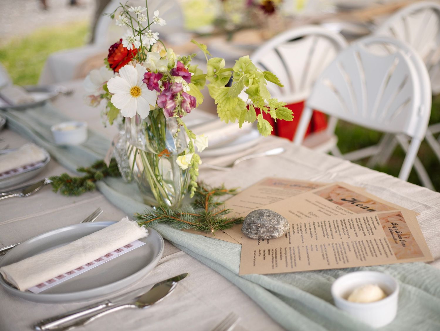 Elegant outdoor wedding table setting with wildflower centerpieces, menu cards, and place settings on a light blue tablecloth.