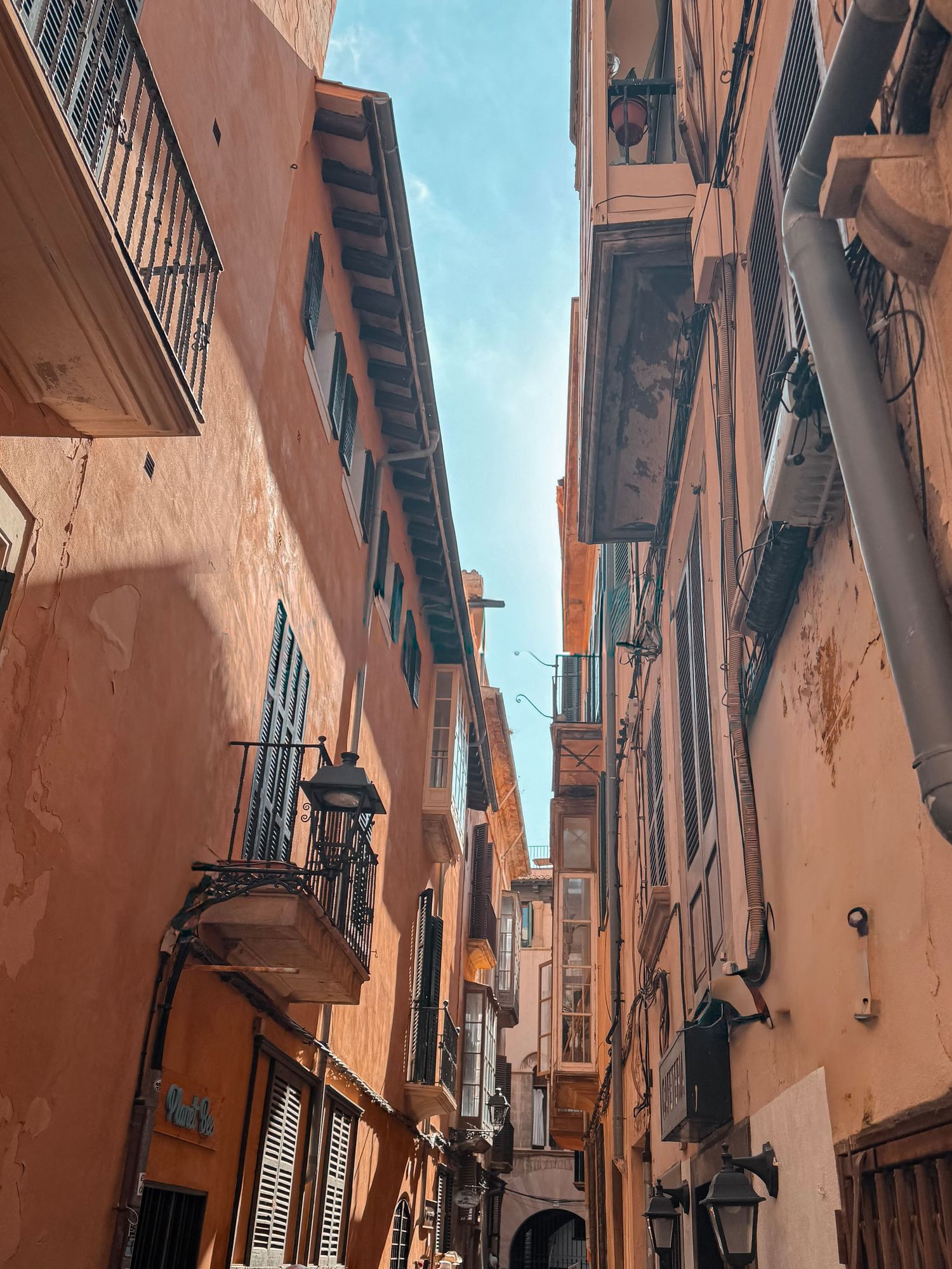 Narrow streets of Alfama district in Lisbon with rustic orange buildings and traditional balconies against blue sky.