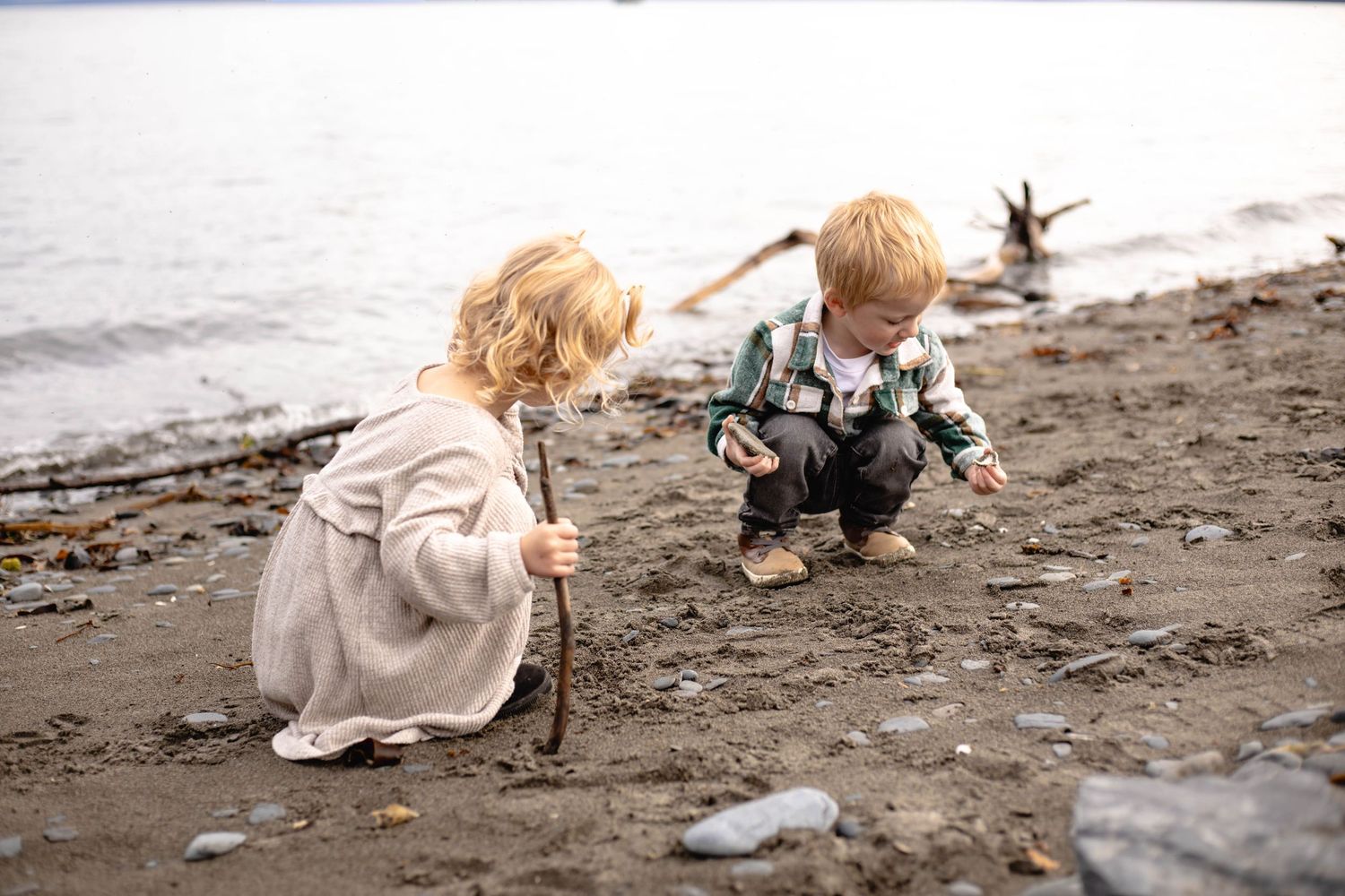 A child plays in the sand and rocks along a misty waterfront.
