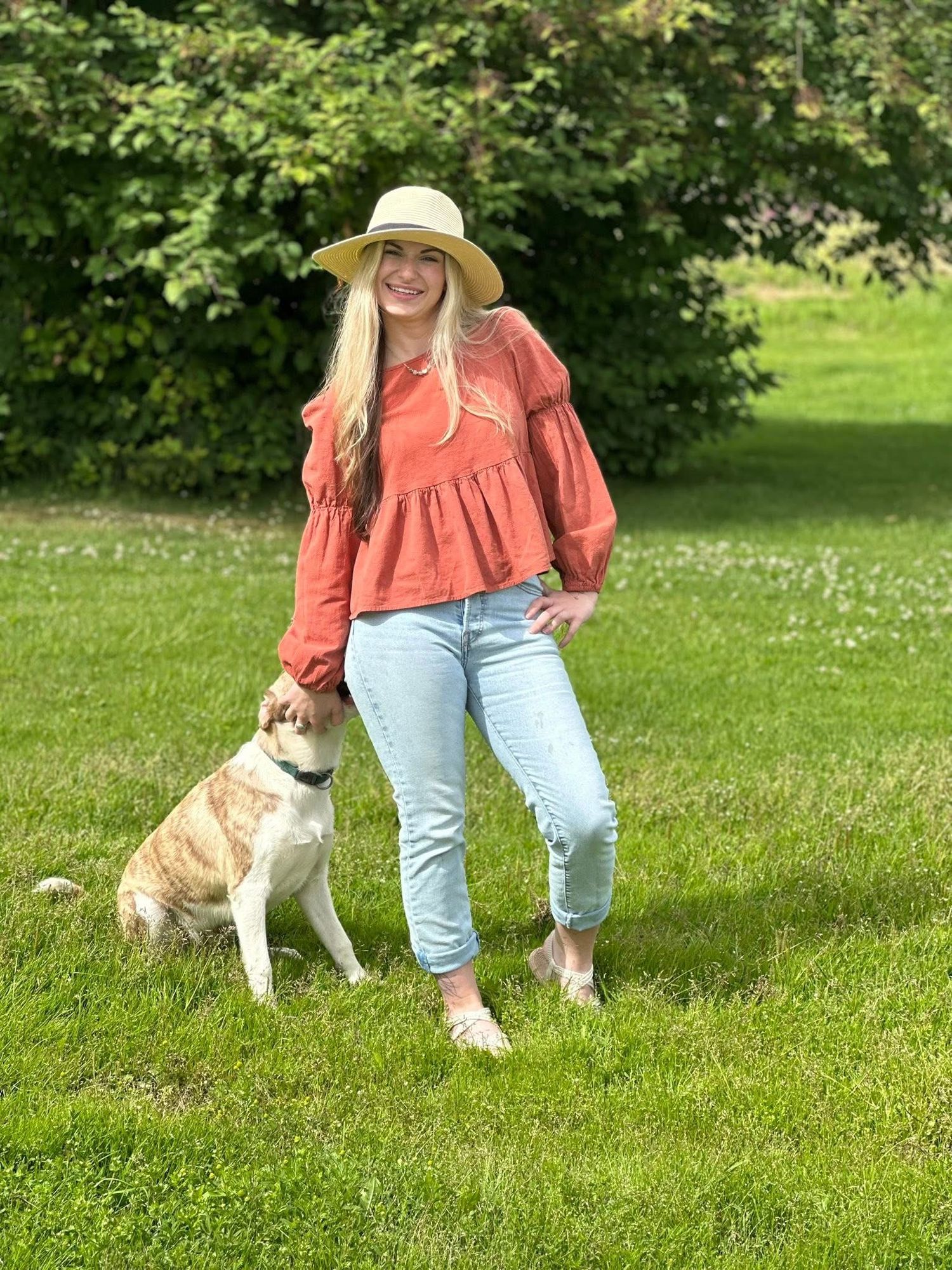Person in coral top and jeans walking with dog in sunny green park.