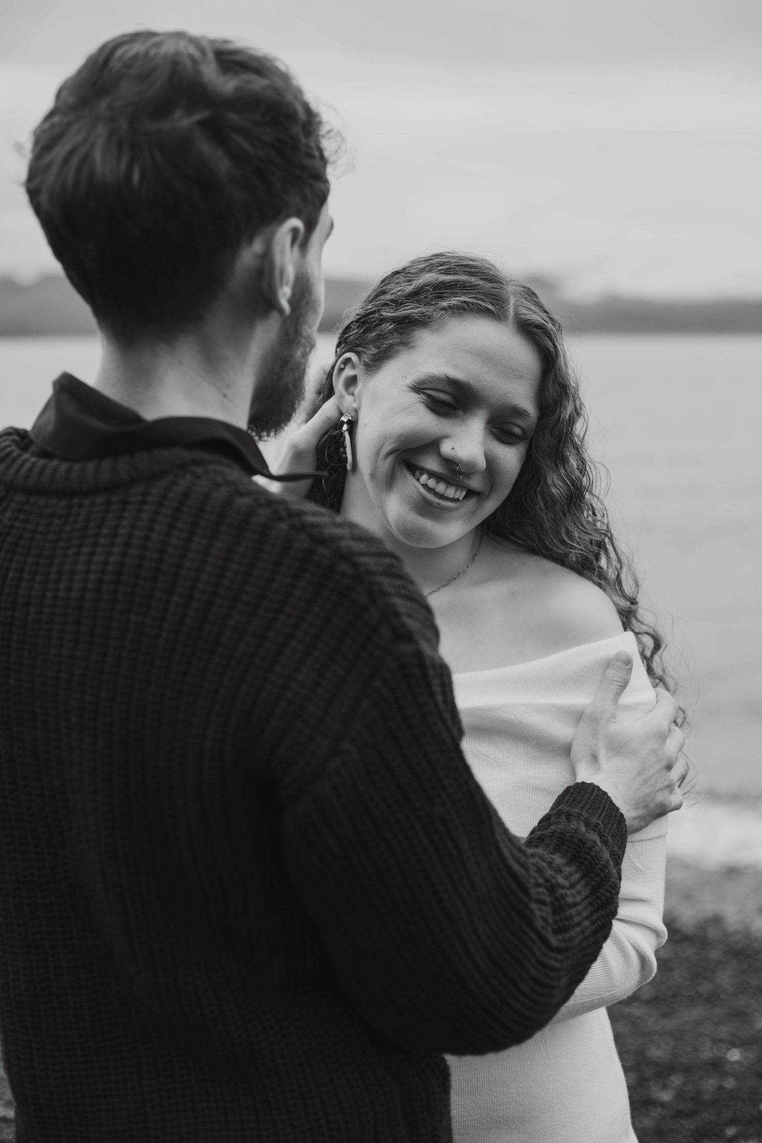 A romantic black and white photo sequence showing a couple embracing on a moody beach shoreline.
