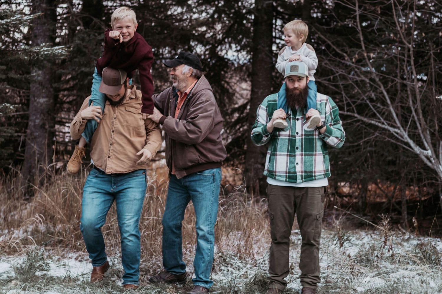 Three men with children on their shoulders walk outdoors in a snowy forest setting during a family winter outing.
