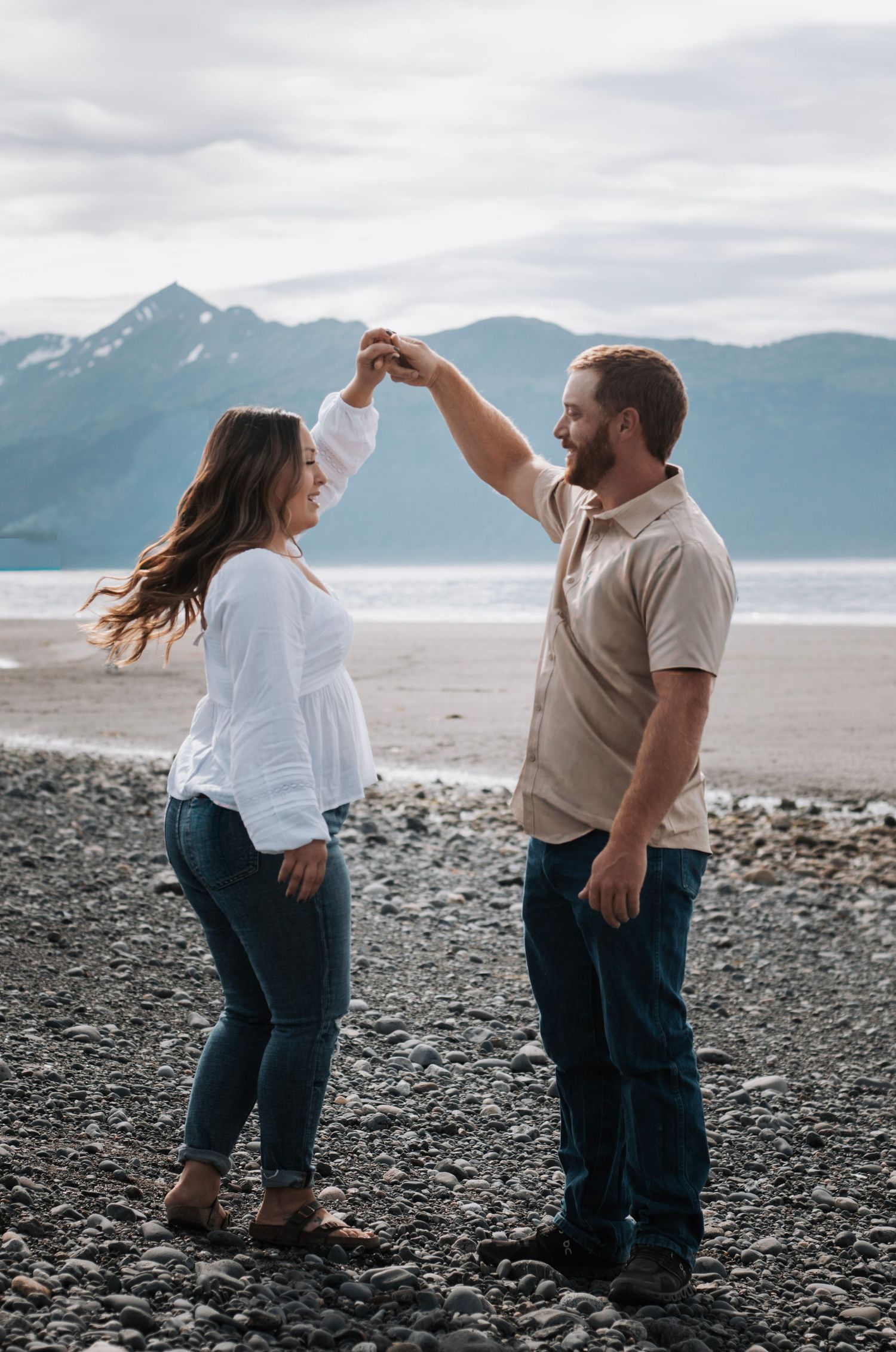 A couple dancing together on an Alaskan beach with snow-capped mountains in the background.
