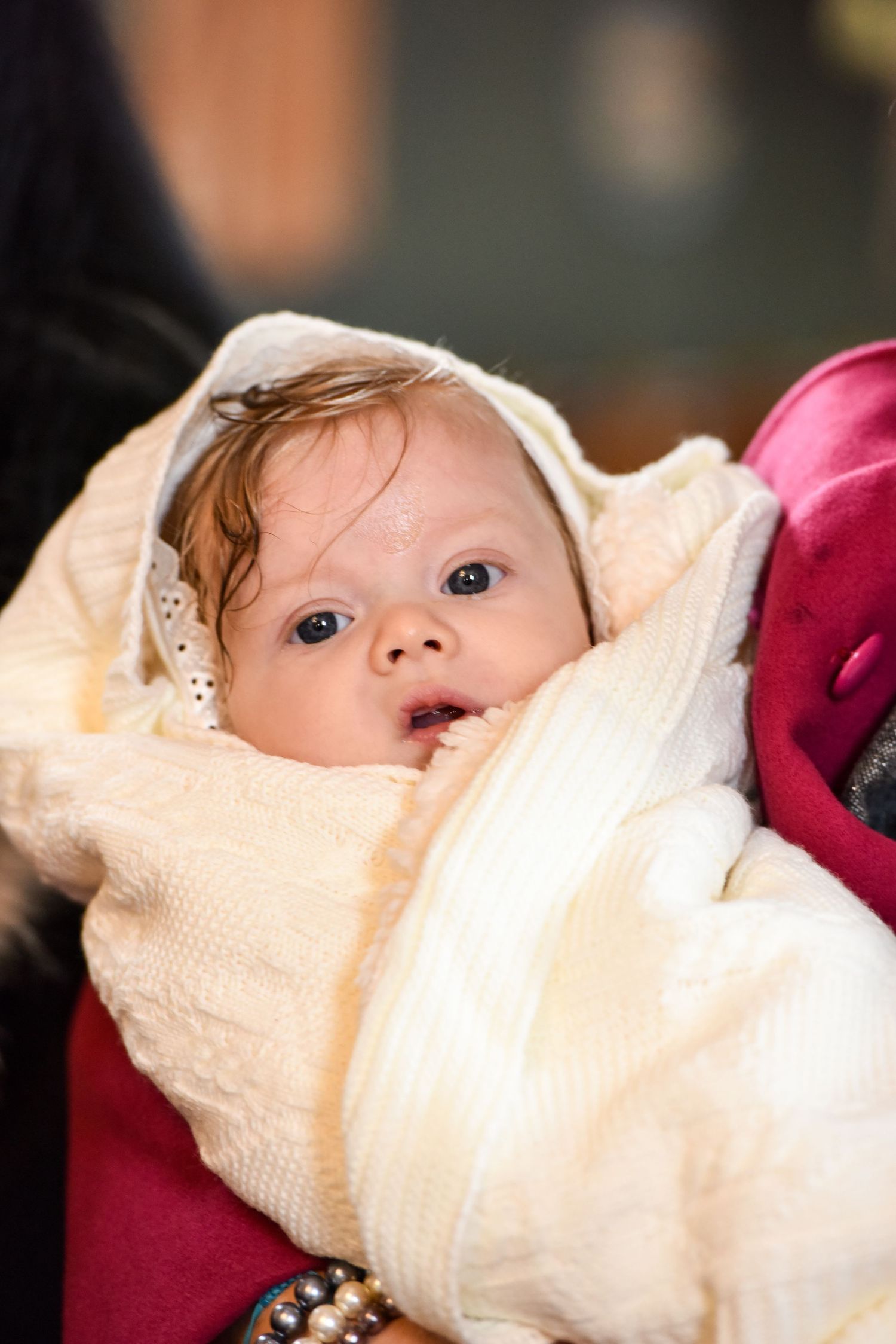 Newborn baby wrapped in white knit blanket with wet hair after baptism ceremony.
