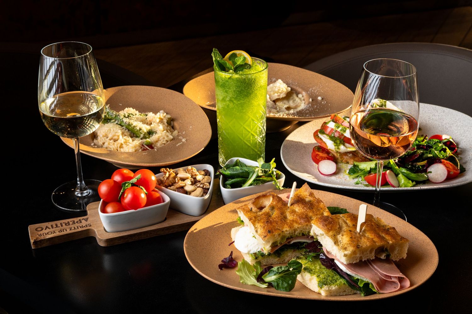 A spread of Italian dishes including pasta, bruschetta, salad, and drinks on a dark restaurant table.