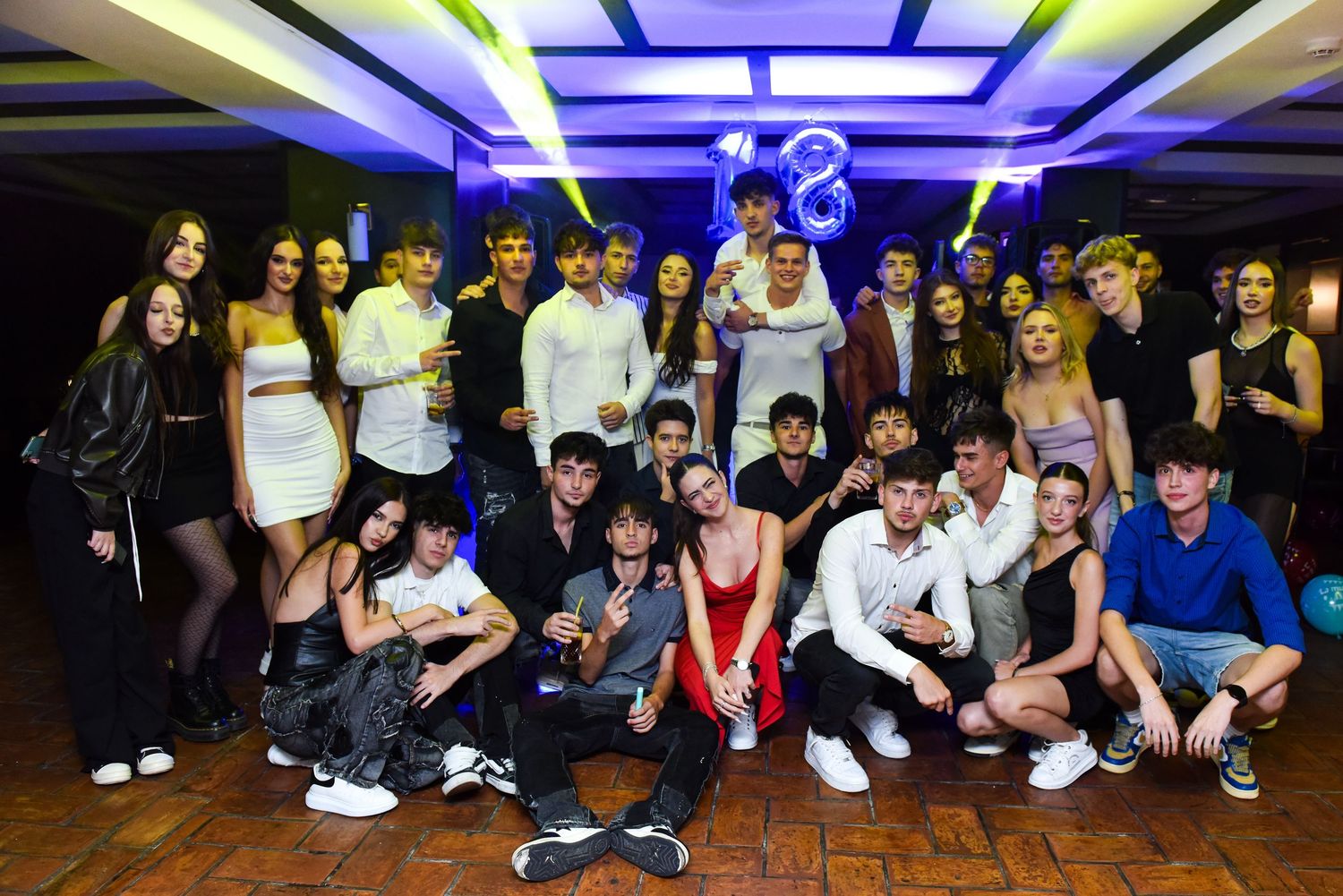 Large group of teens posing together at an 18th birthday party celebration in a decorated venue.