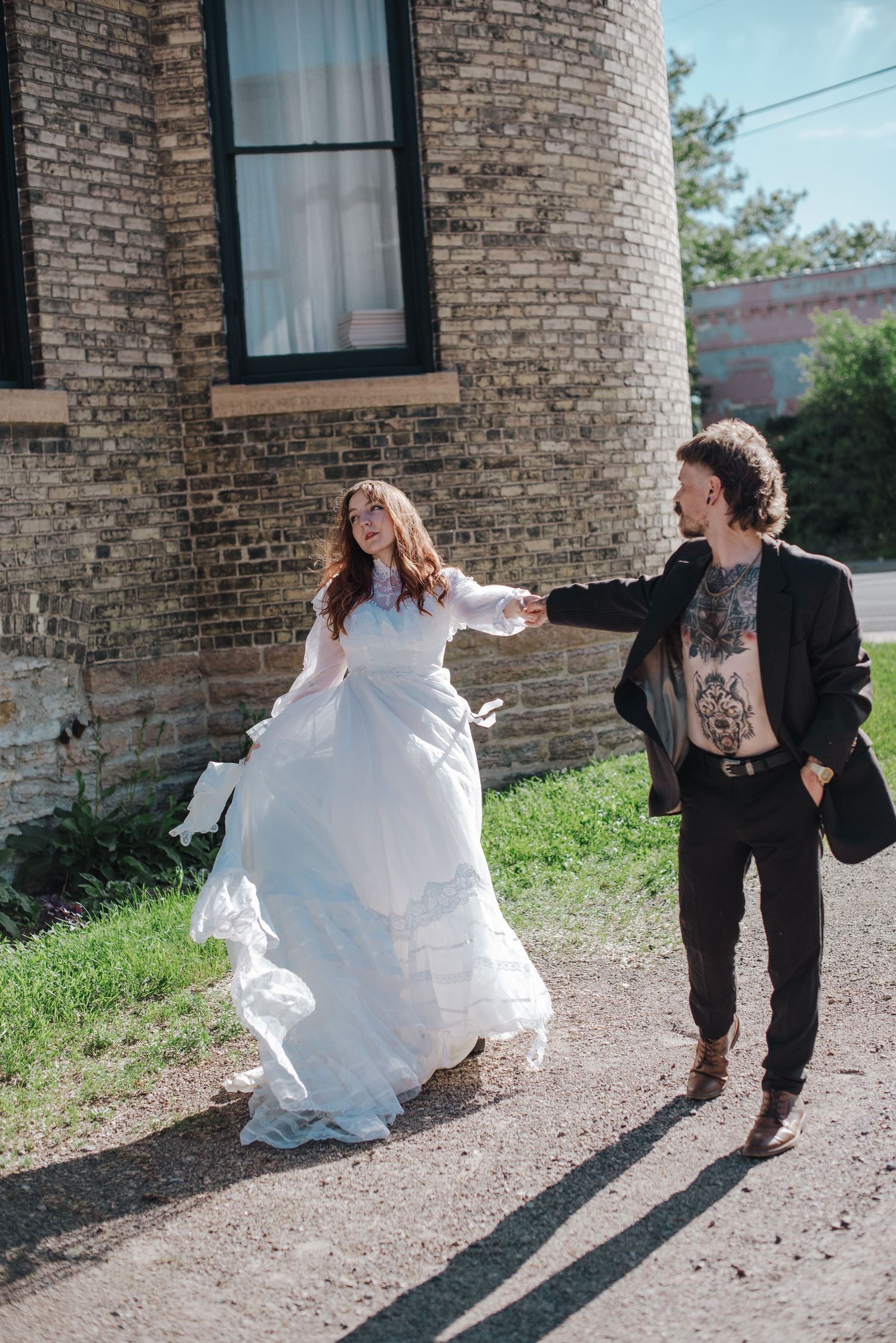 Wedding couple walks hand-in-hand past a stone brick building on a sunny day in Minneapolis, Minnesota