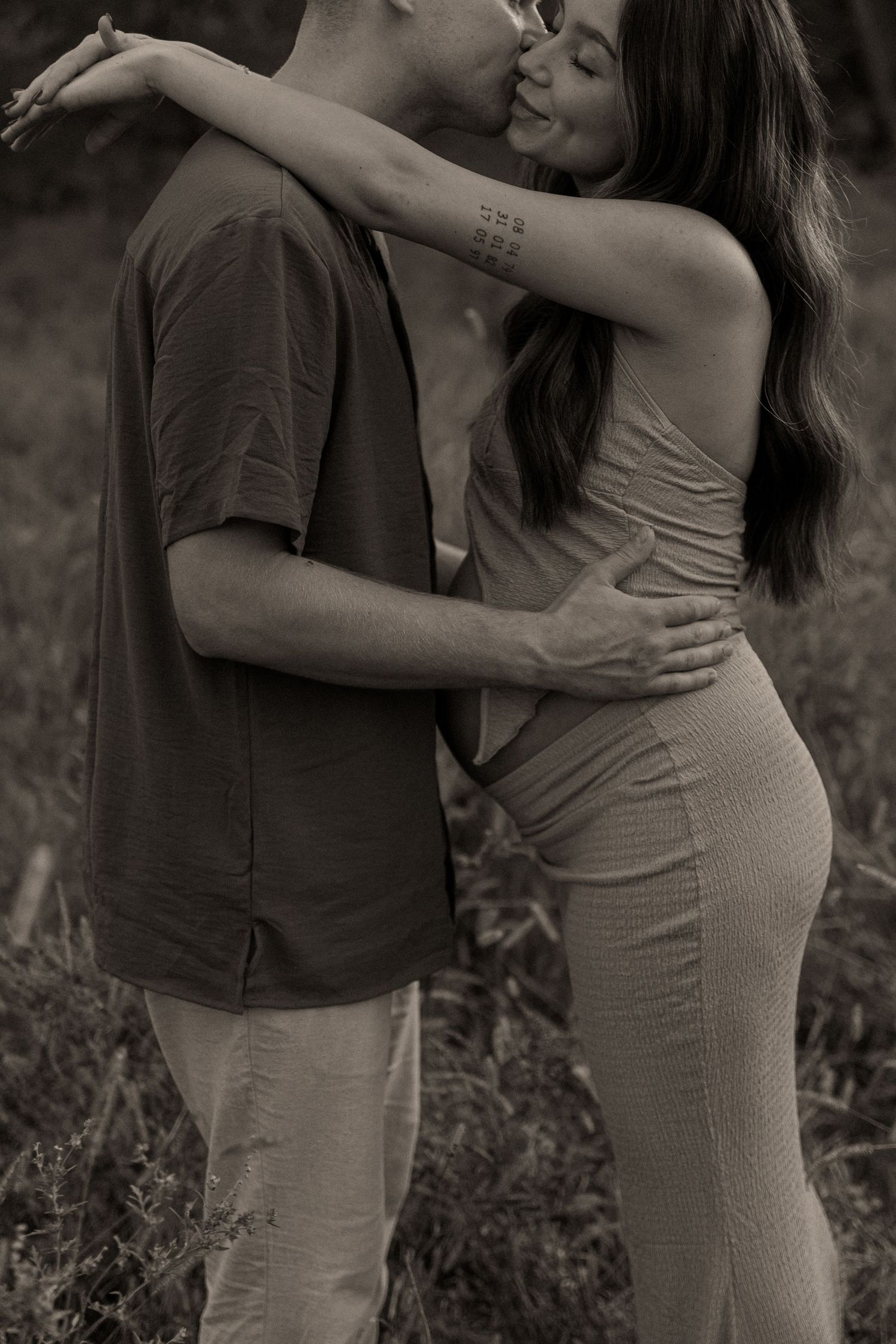 Intimate black and white maternity photo of couple embracing in field.