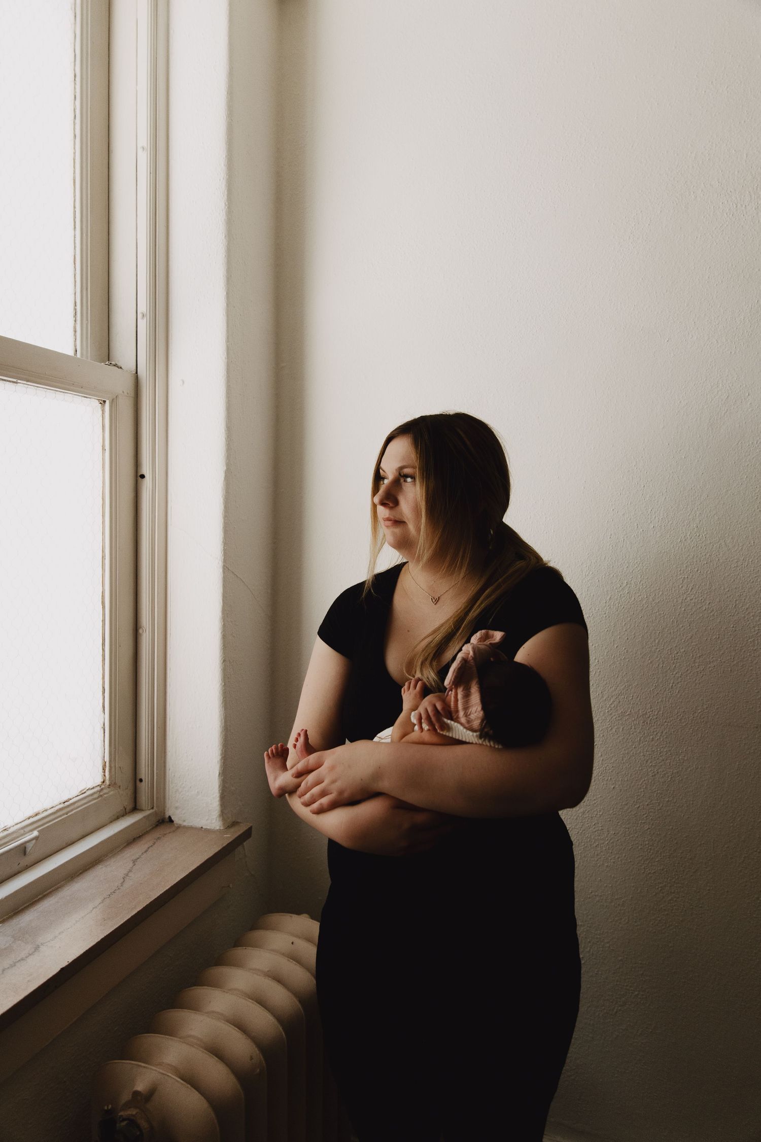 Atmospheric portrait by a bright window creating dramatic contrast and shadows.