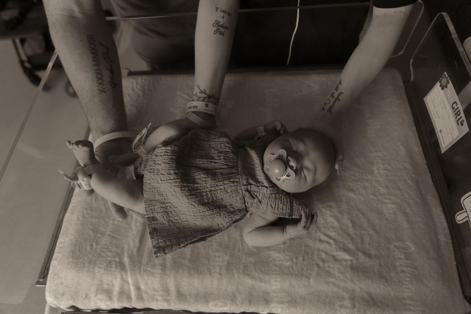 Black and white image of infant lying on bed in hospital setting.