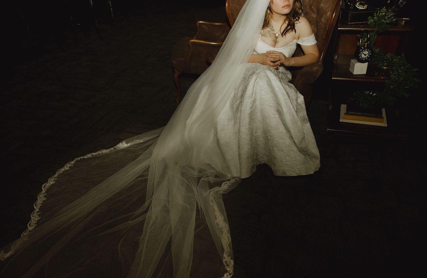 A bride in a flowing white wedding gown poses in dramatic lighting against a dark background.
