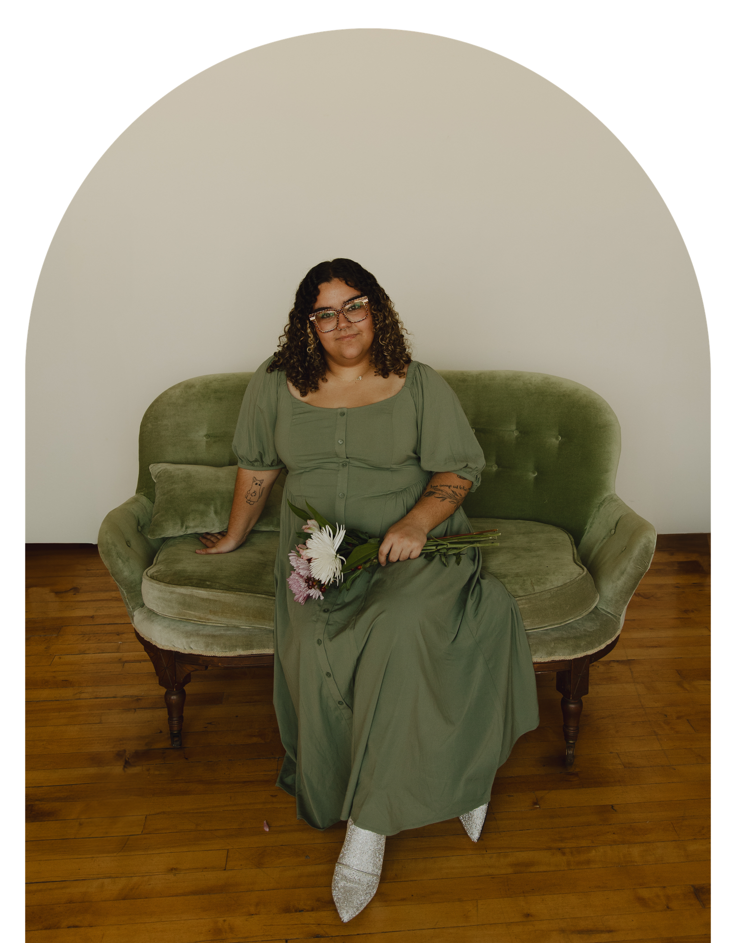 Wedding guest relaxing on a vintage green velvet sofa holding a floral bouquet.