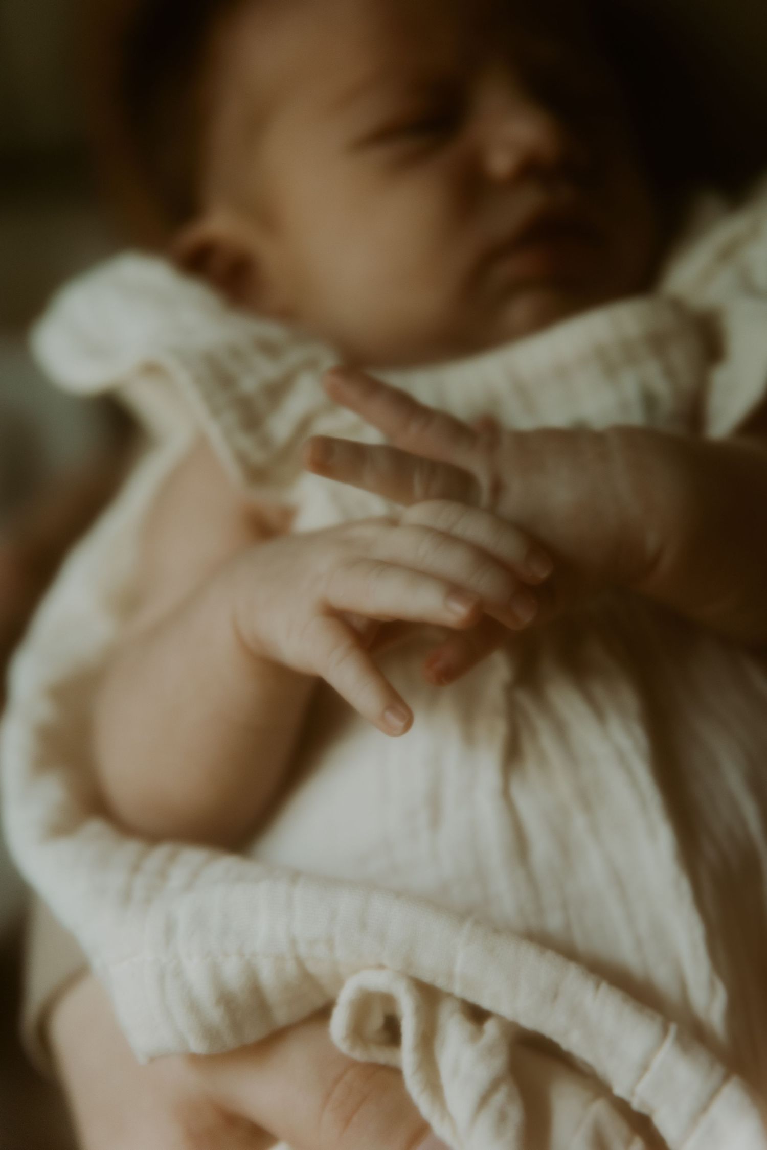 Soft focus detail of a baby wrapped in white cloth showing delicate skin and tiny features.
