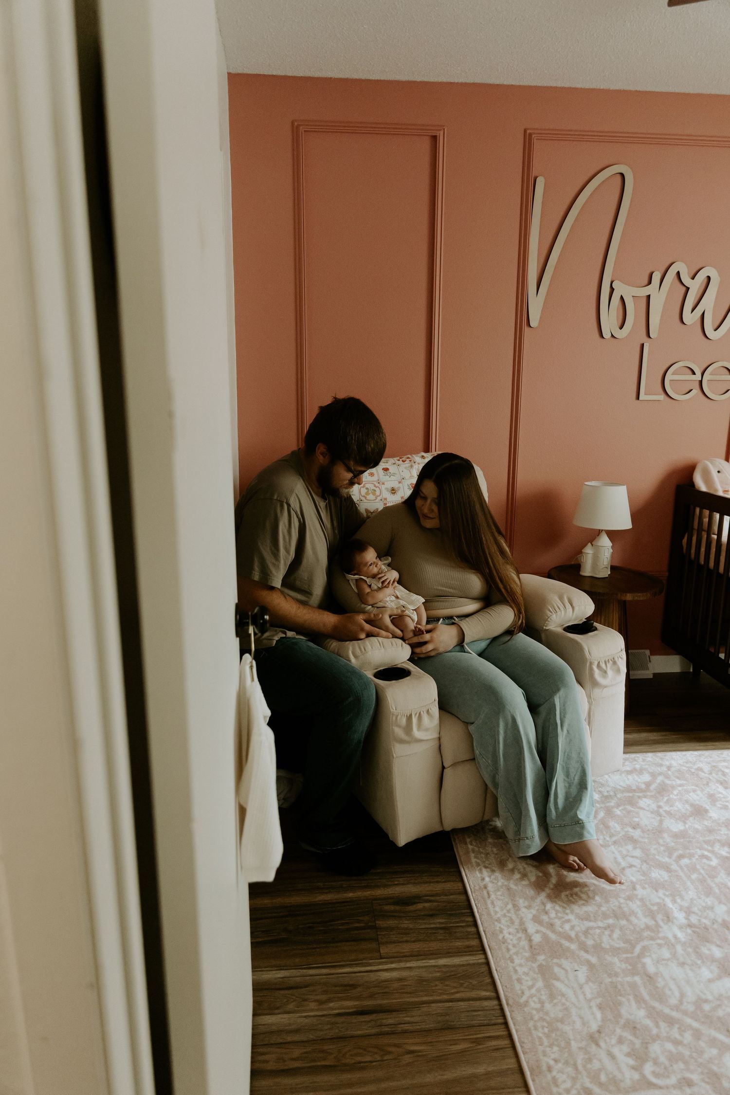 Intimate family moment captured on a couch in a room with coral-colored walls.