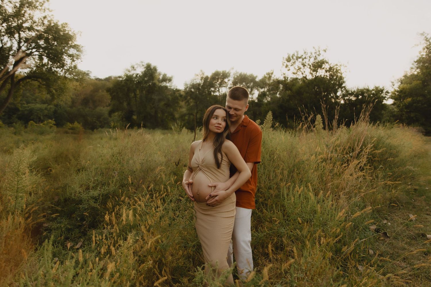 Maternity photo of couple embracing in golden field at sunset.