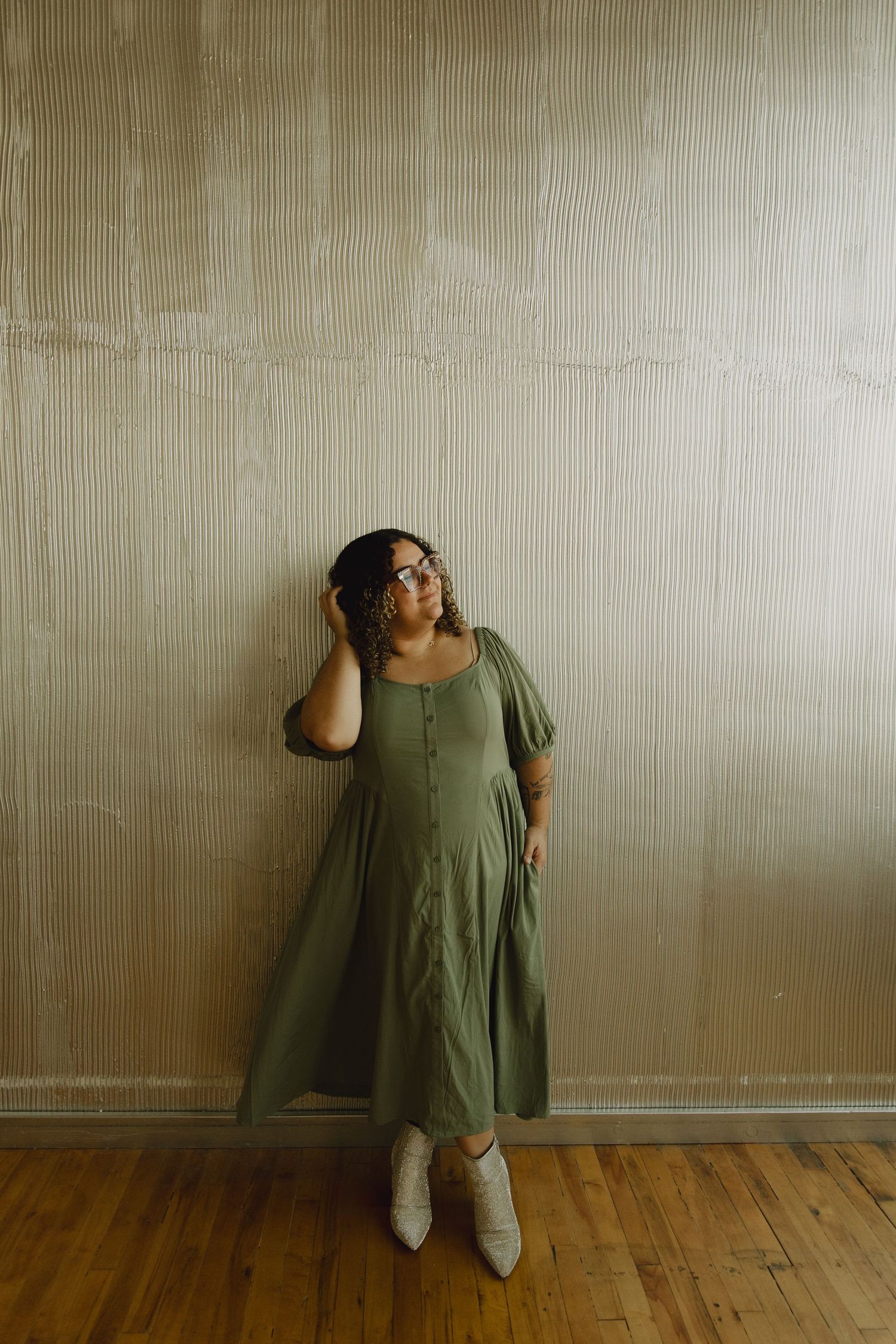 A person in a green dress sits casually against a wall in a room with hardwood floors.