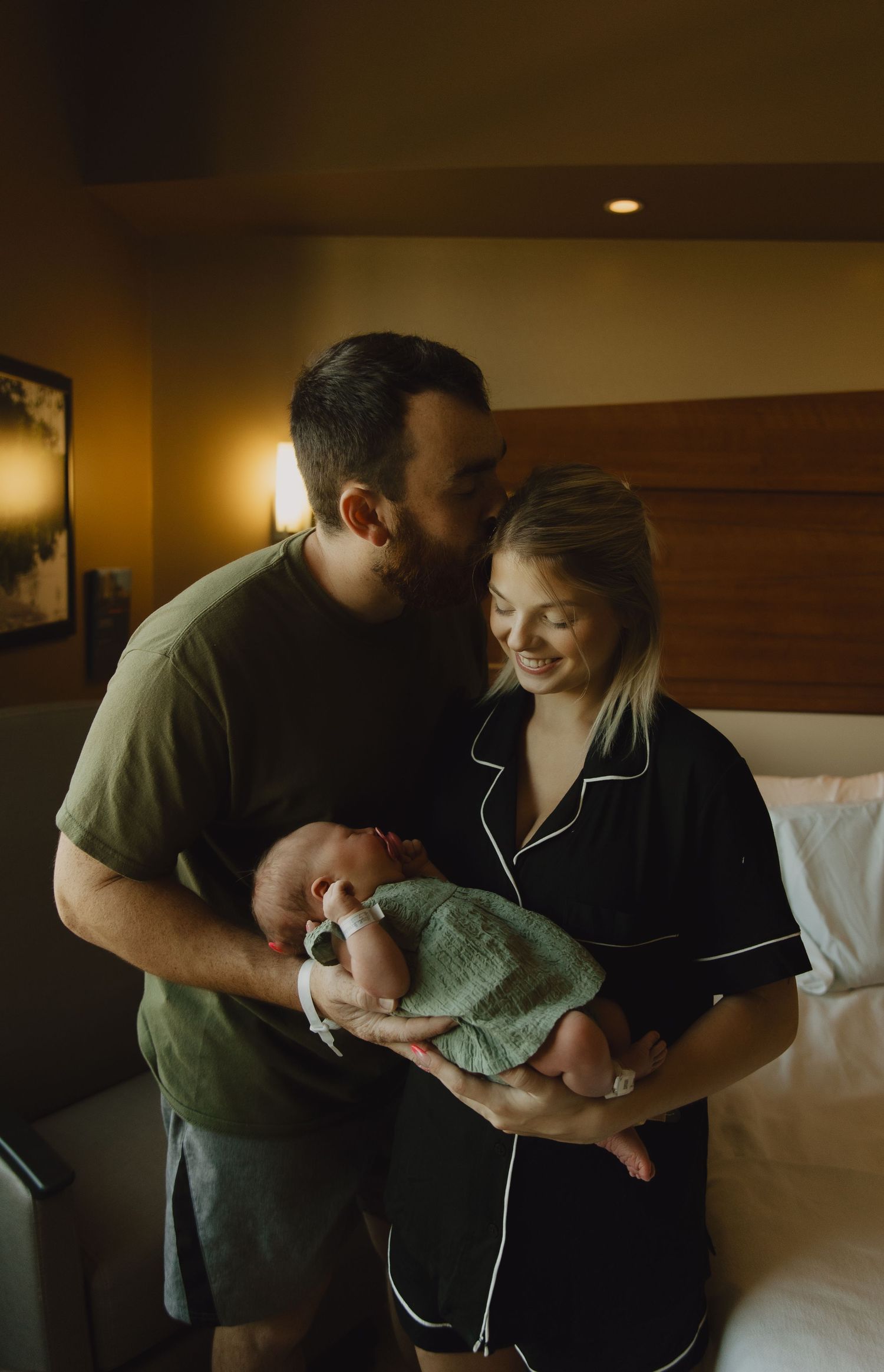 Tender moments captured in a dimly lit bedroom as a newborn is cradled in loving arms.