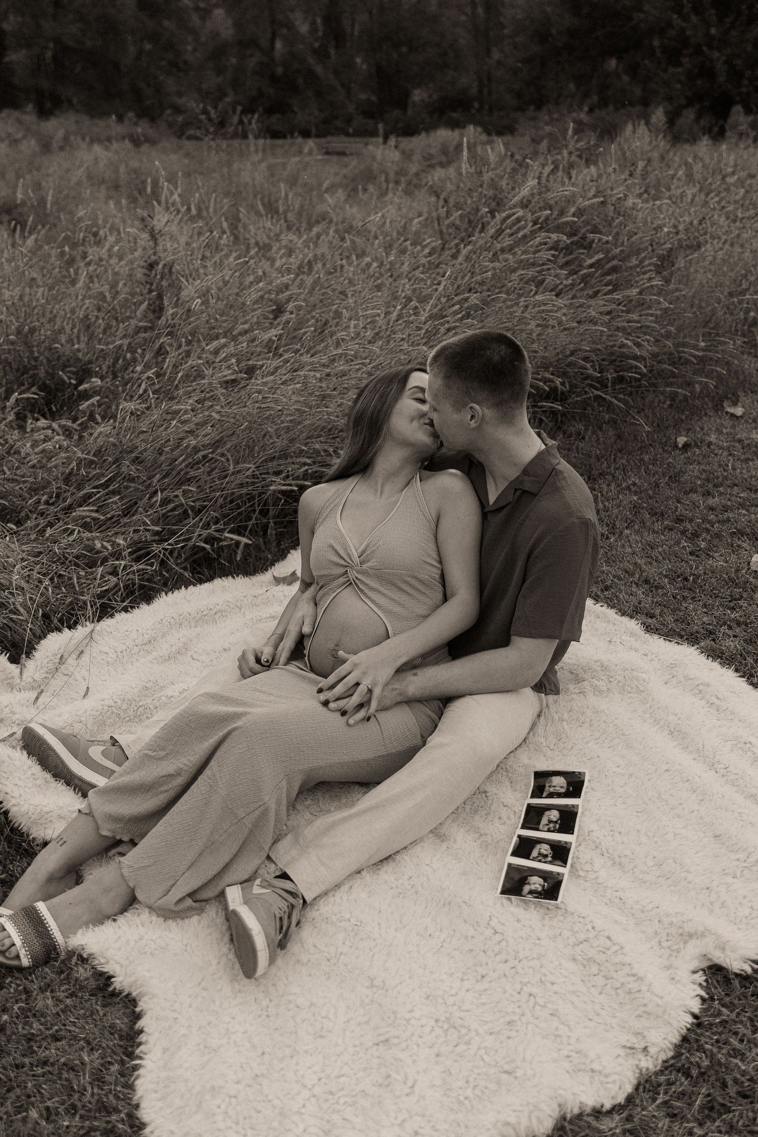 Black and white photo of expecting couple relaxing on blanket with ultrasound photos.