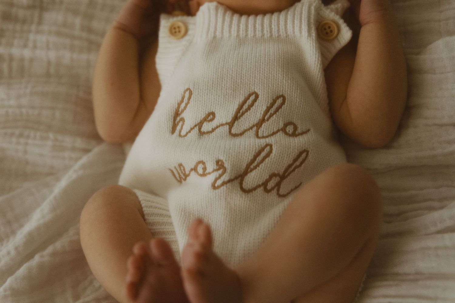 Close-up of white knit baby clothing with embroidered text.