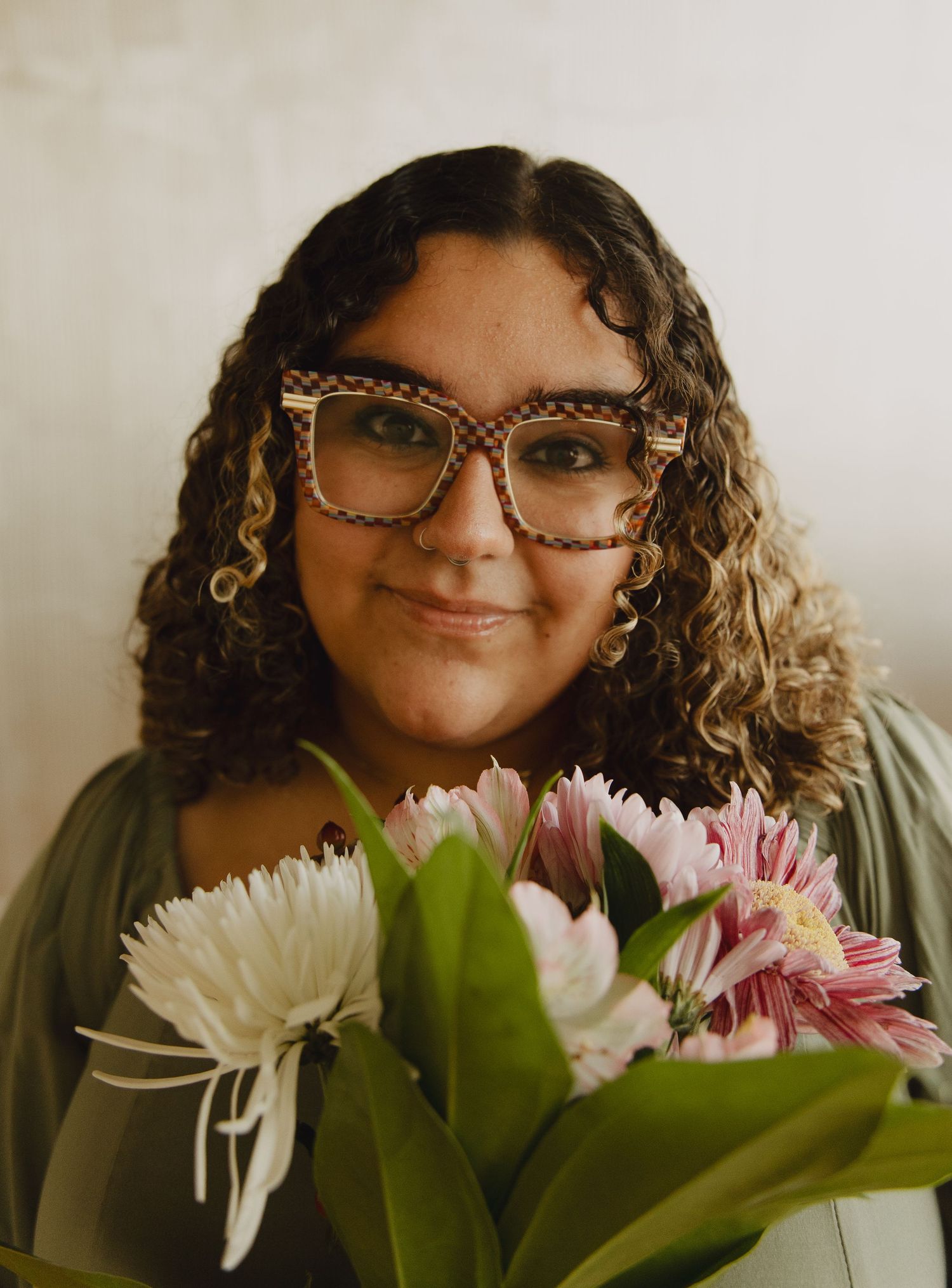 A series of warm-toned portrait shots showing someone with curly hair and glasses posing with white and pink flowers.