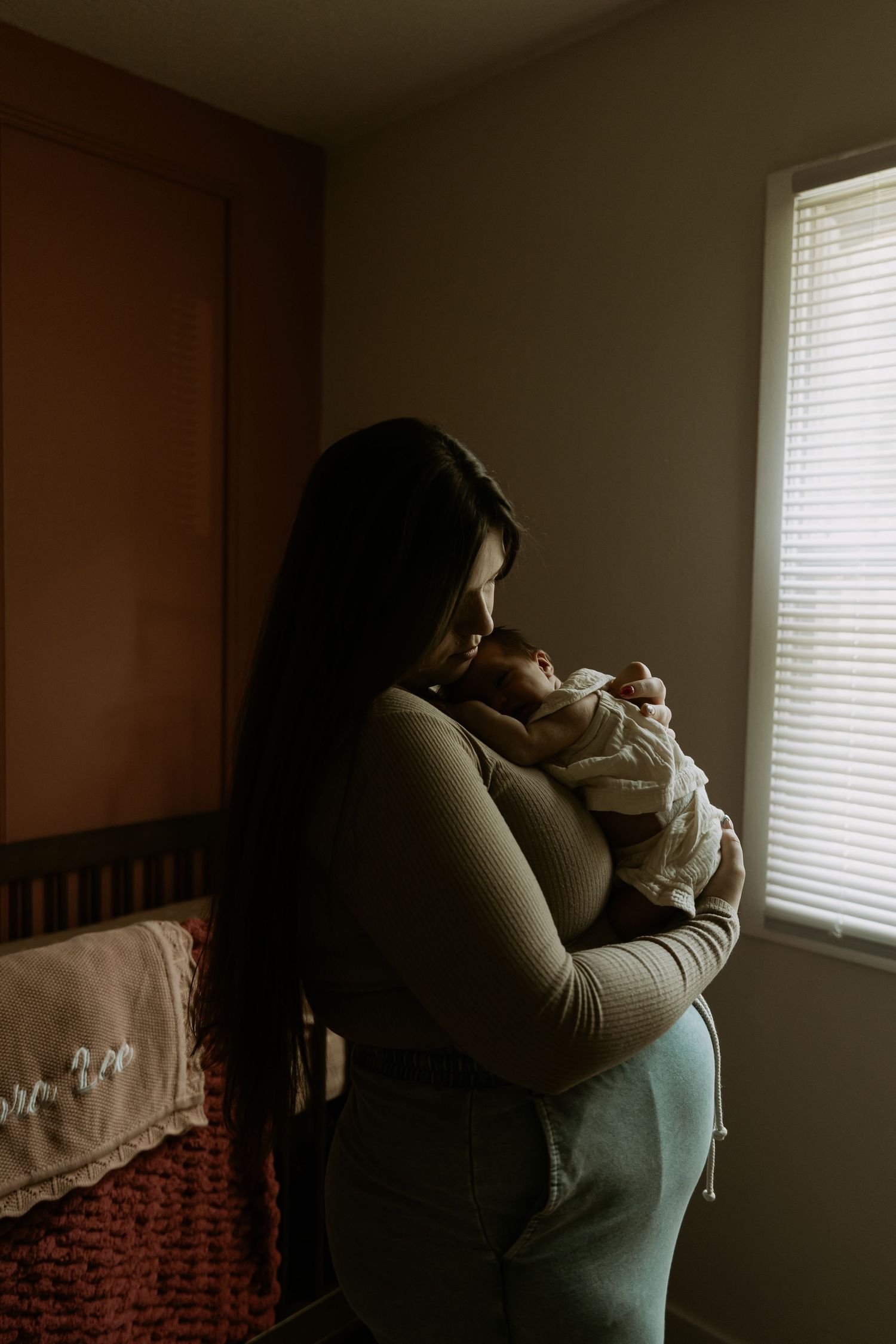 A series of moody photographs showing a person in dim lighting by a window holding a small baby.