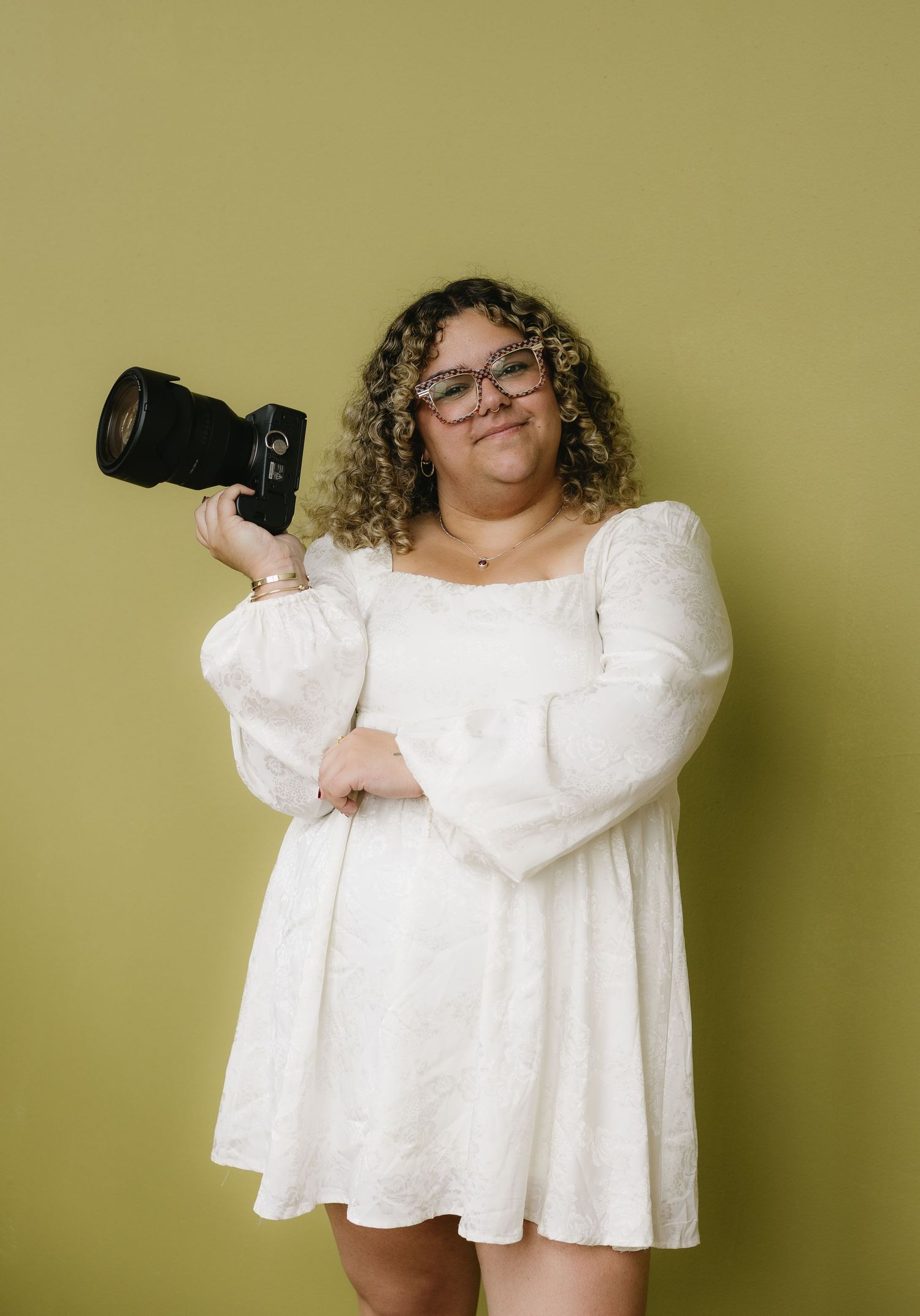 Woman in white dress holding a camera against green background.