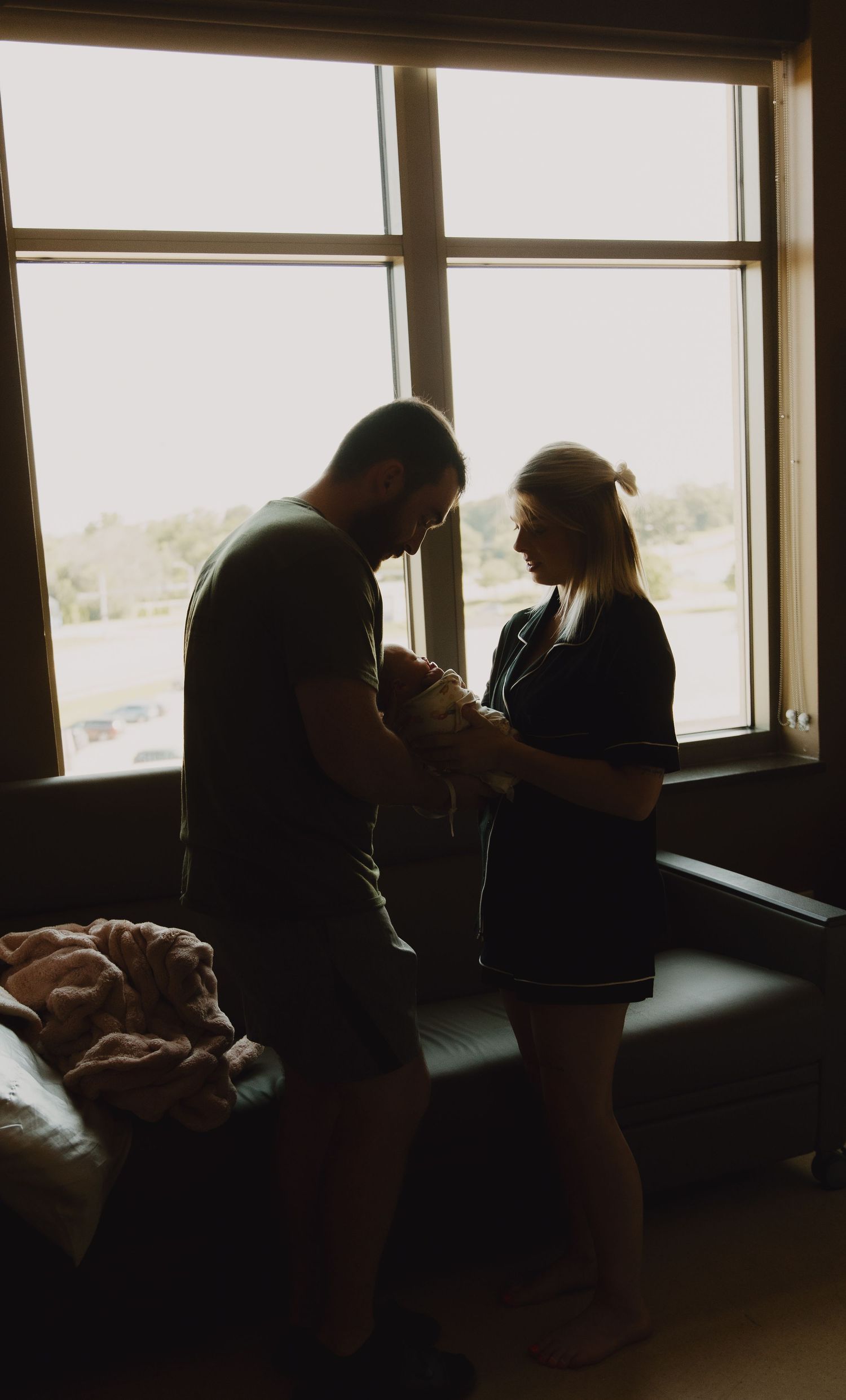 Silhouetted figures stand by large windows in a dimly lit room creating a dramatic atmosphere.