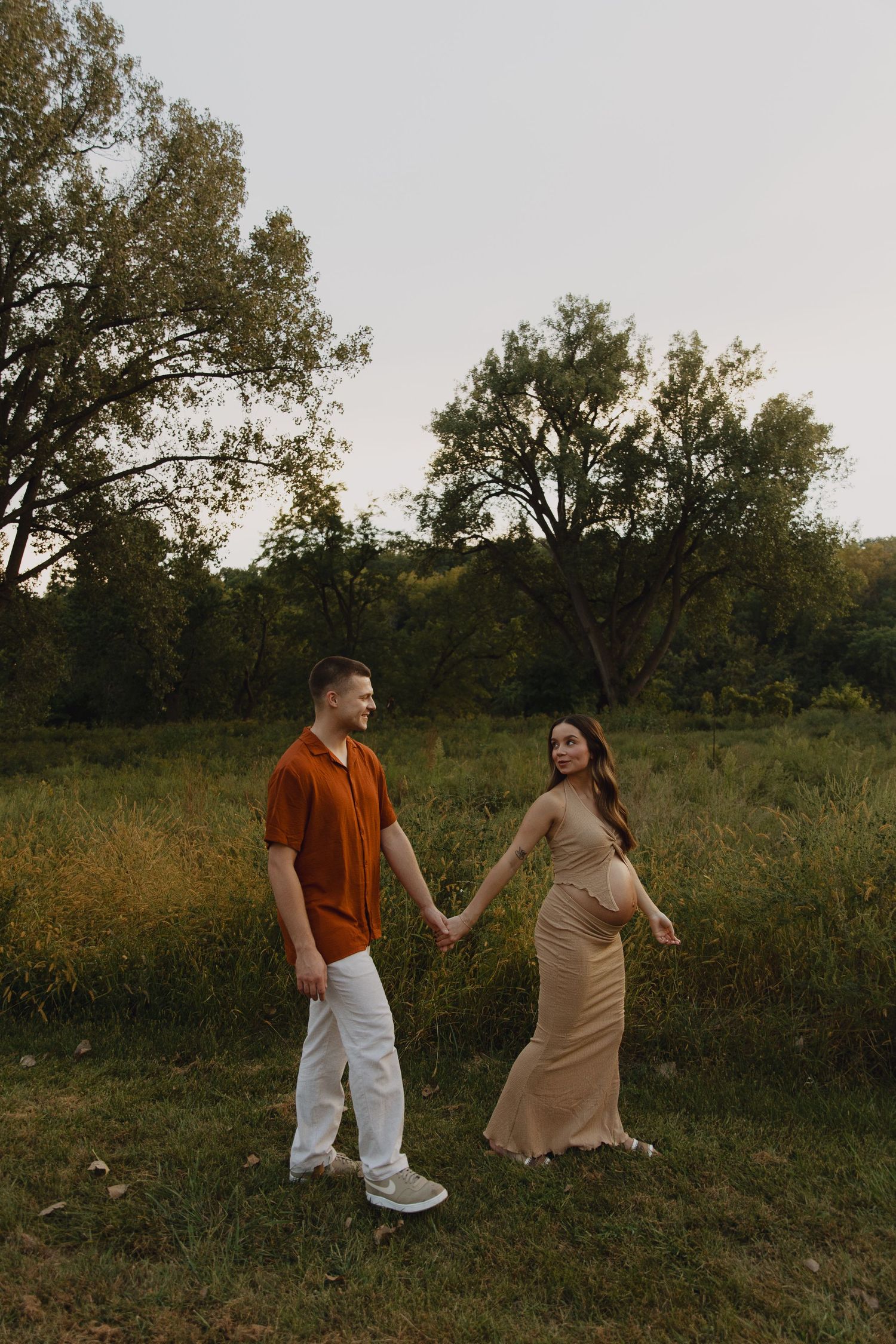 Couple holding hands while walking through scenic field at sunset.