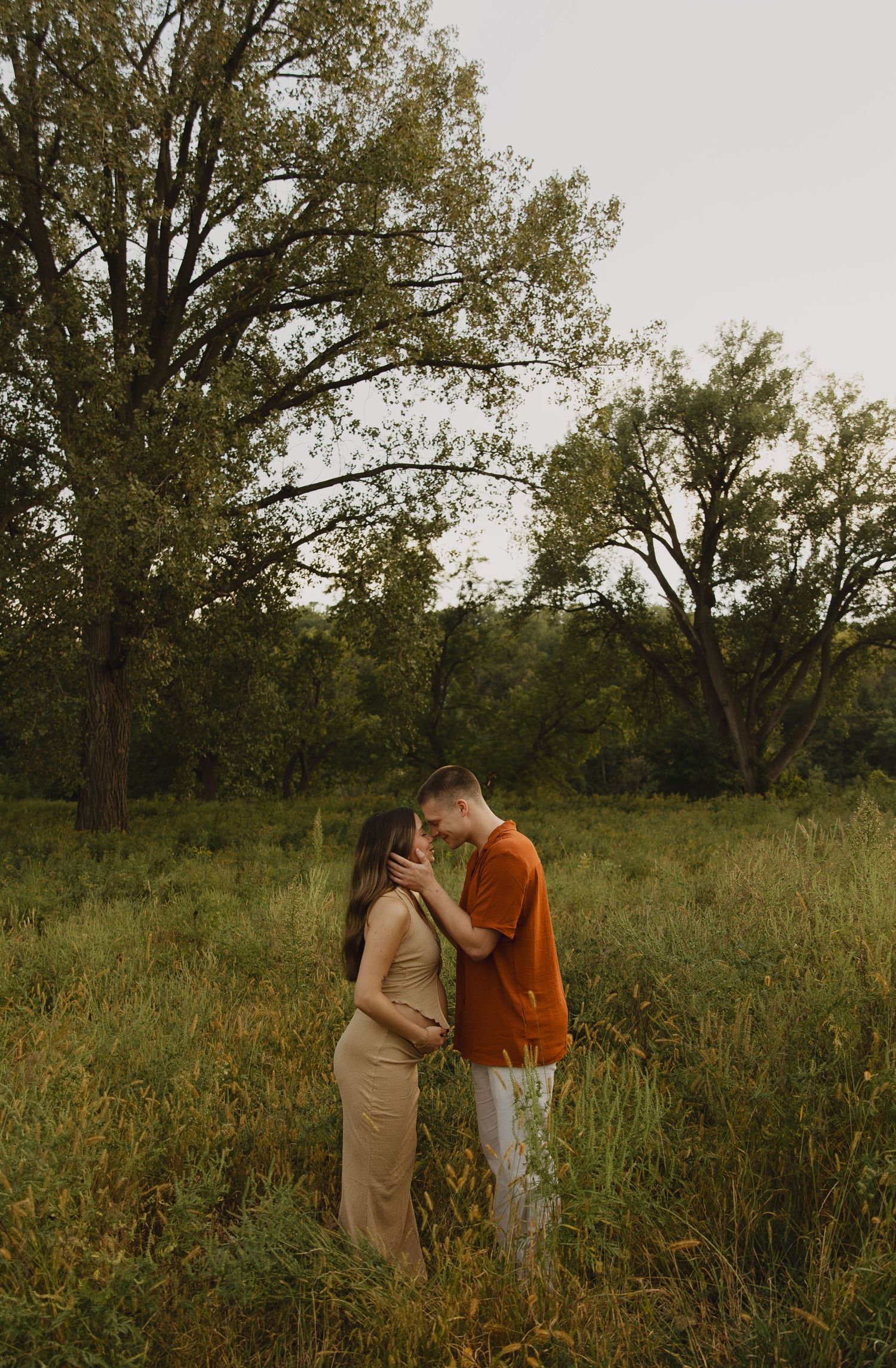 Intimate maternity photo of couple embracing in tall grass during golden hour.