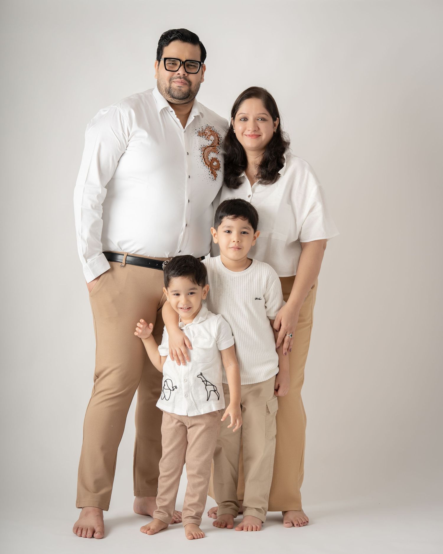 Family of four standing together in coordinated white shirts and tan pants for a studio photo.