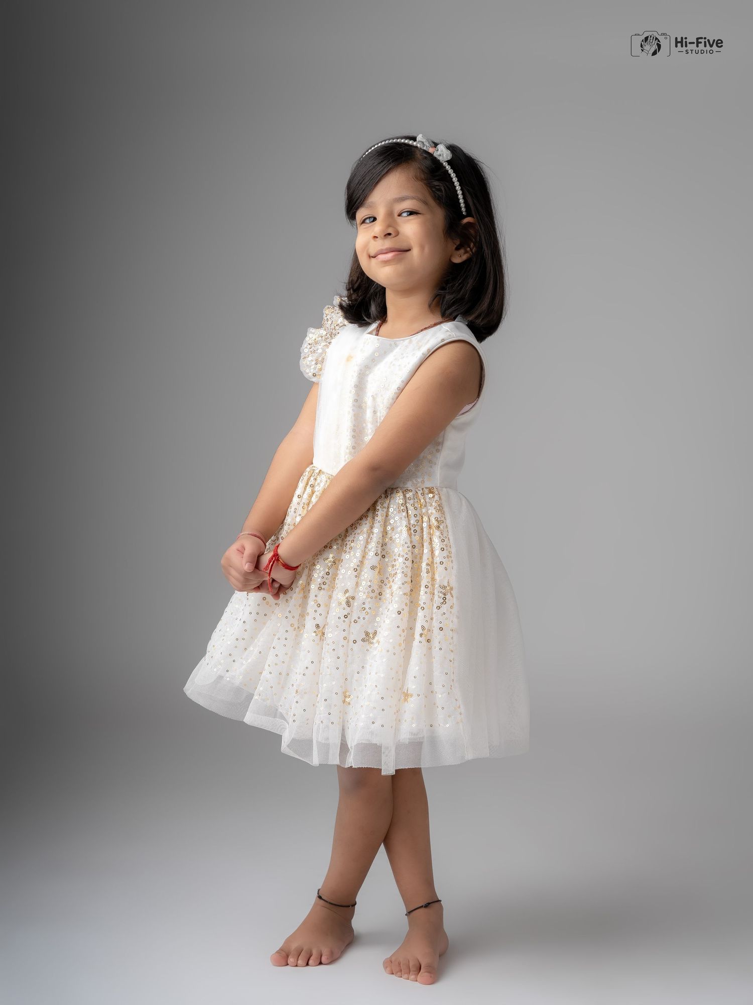 Charming young Indian girl in a white and gold sparkle dress smiles in a professional studio portrait.