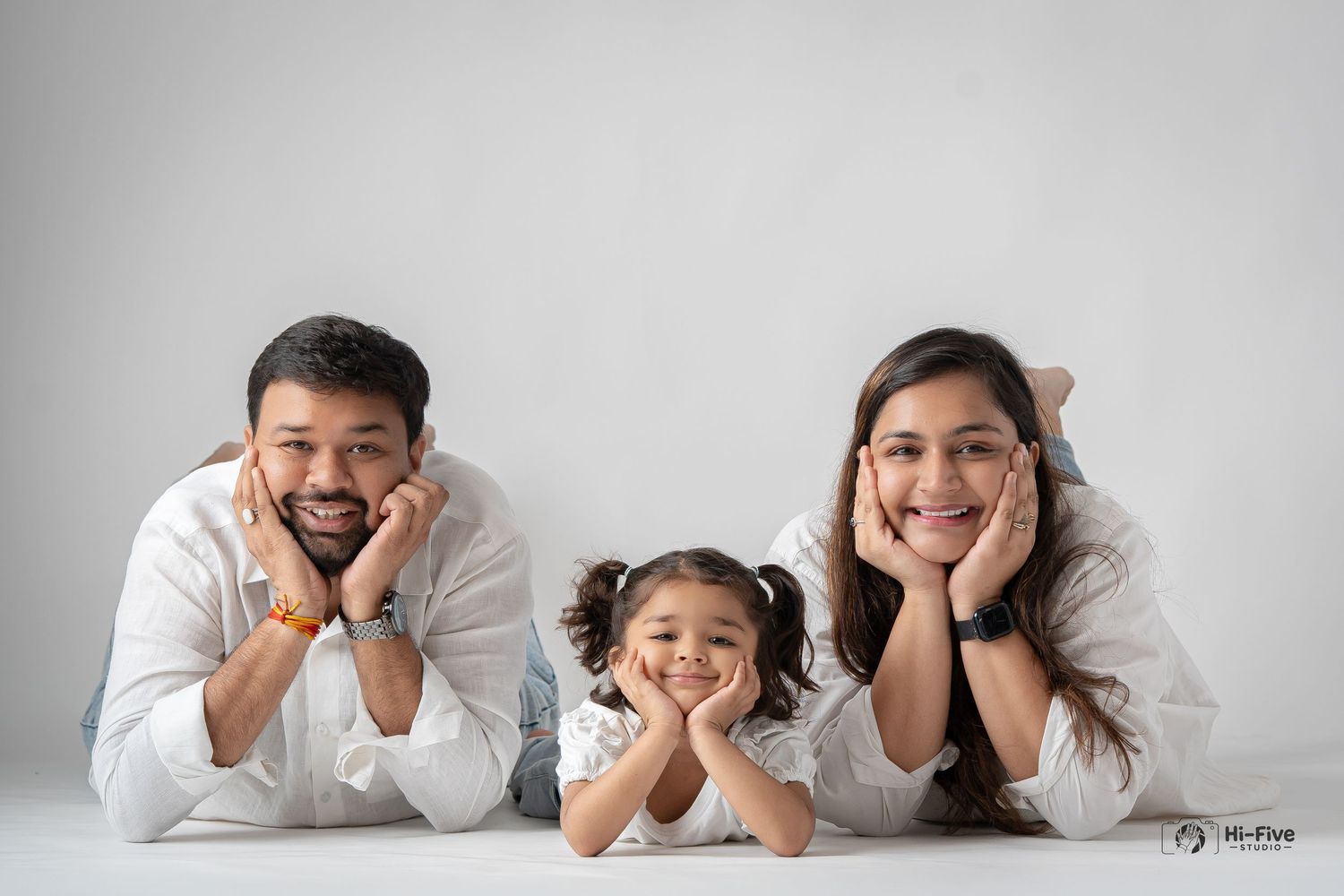 Family of three lying on floor smiling, parents in white shirts with young daughter between them.