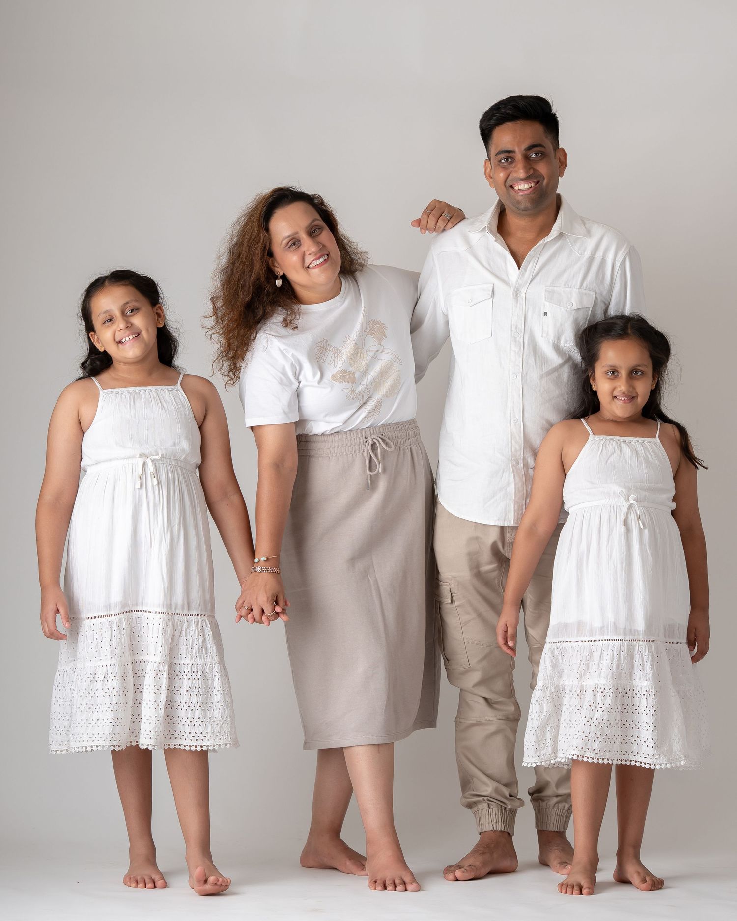 Family of four in coordinating white and beige outfits standing together in a studio portrait.