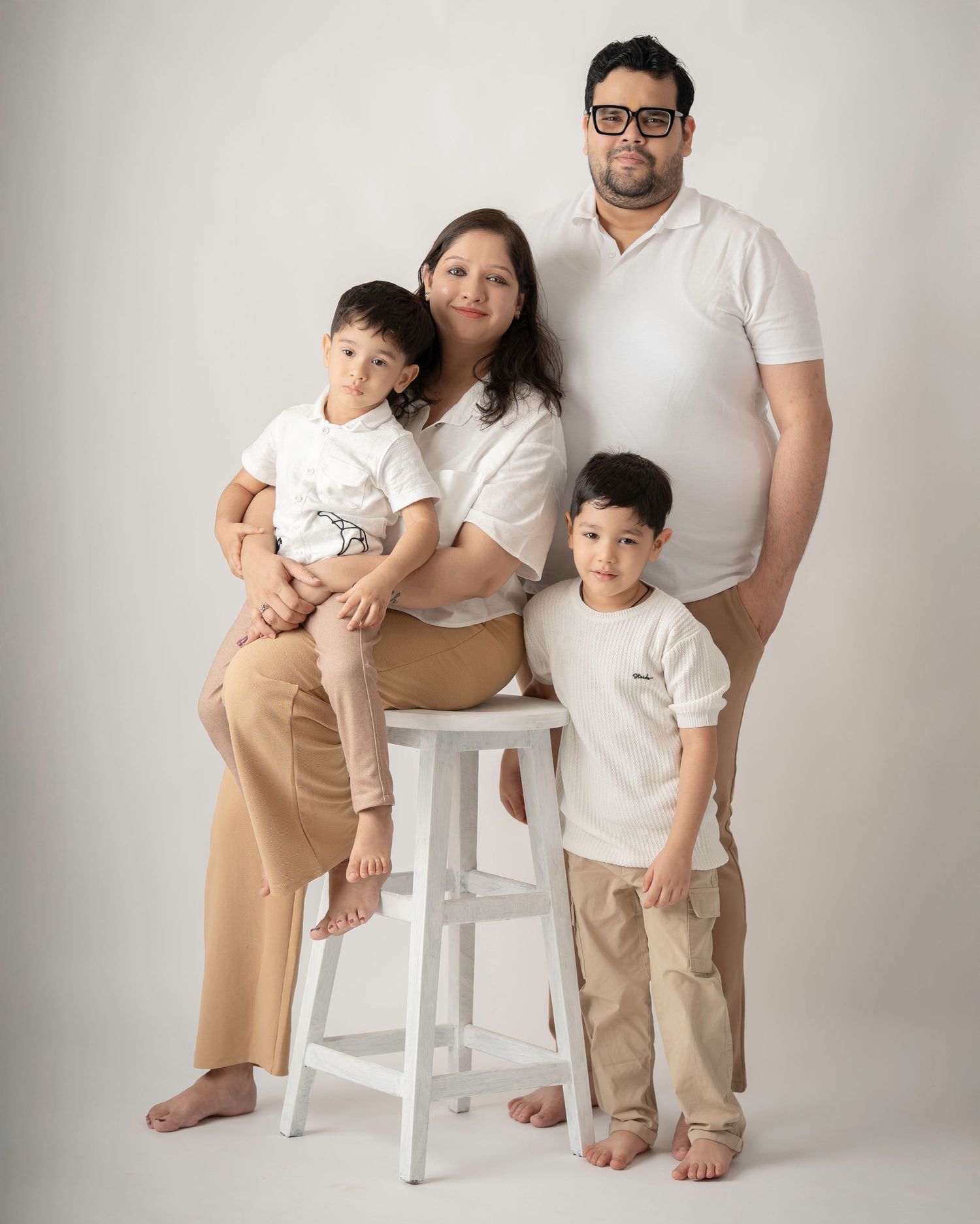 Family of four in white tops and khaki pants posing with a white stool in a studio setting.