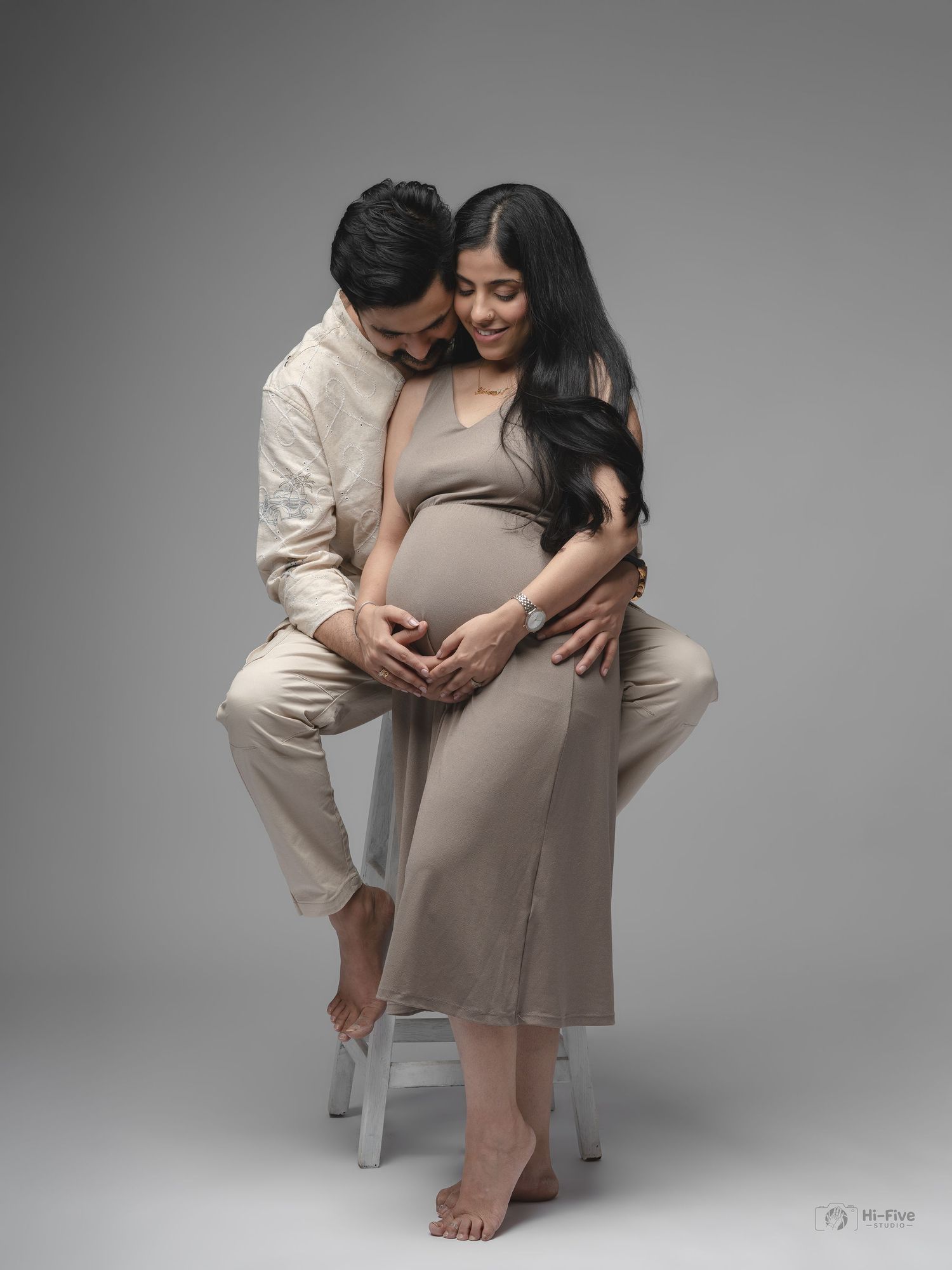 Couple sharing tender moment over pregnant belly, forming heart shape in professional maternity studio.