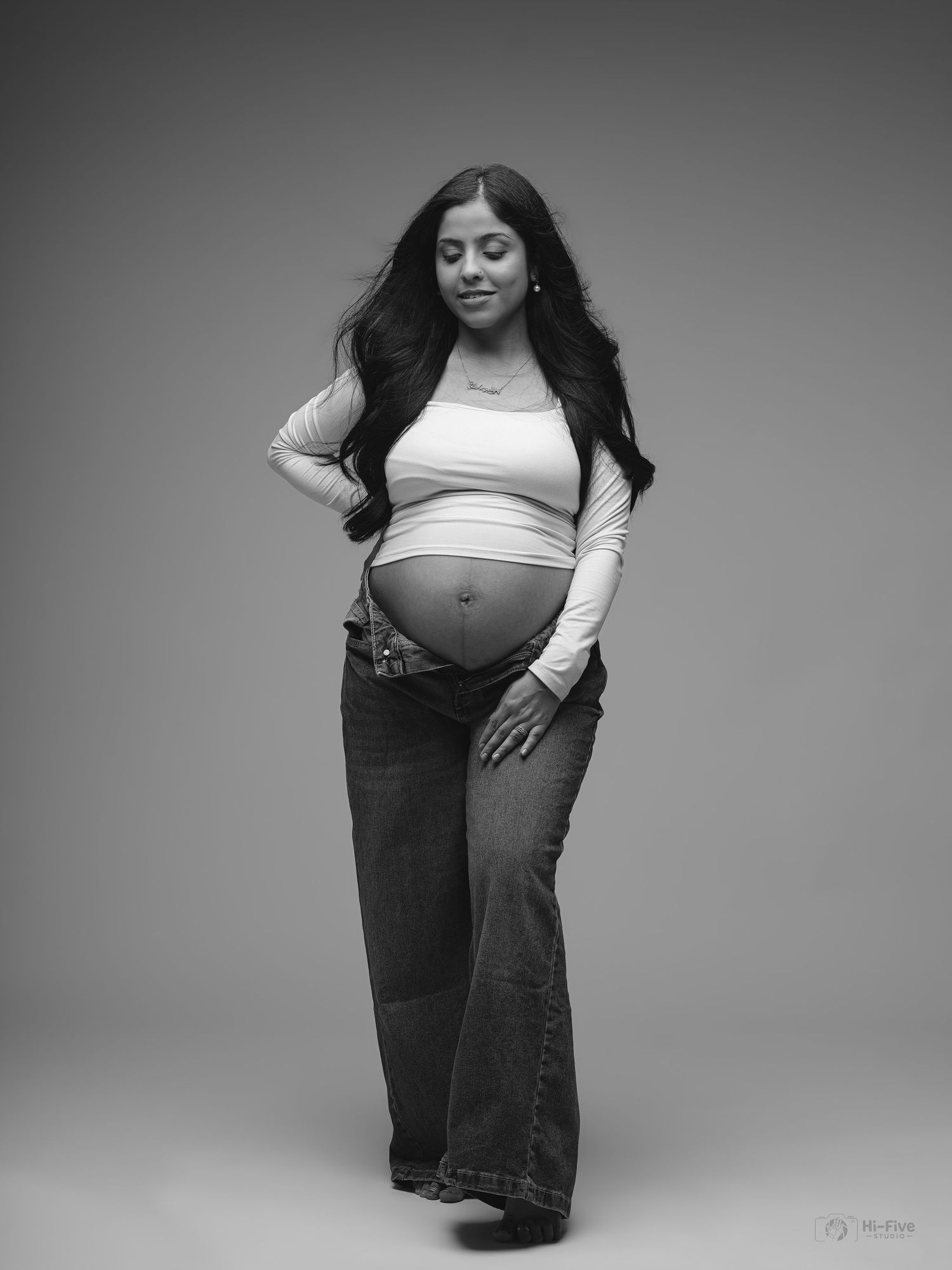 Black and white maternity portrait of pregnant woman in crop top and jeans cradling baby bump.