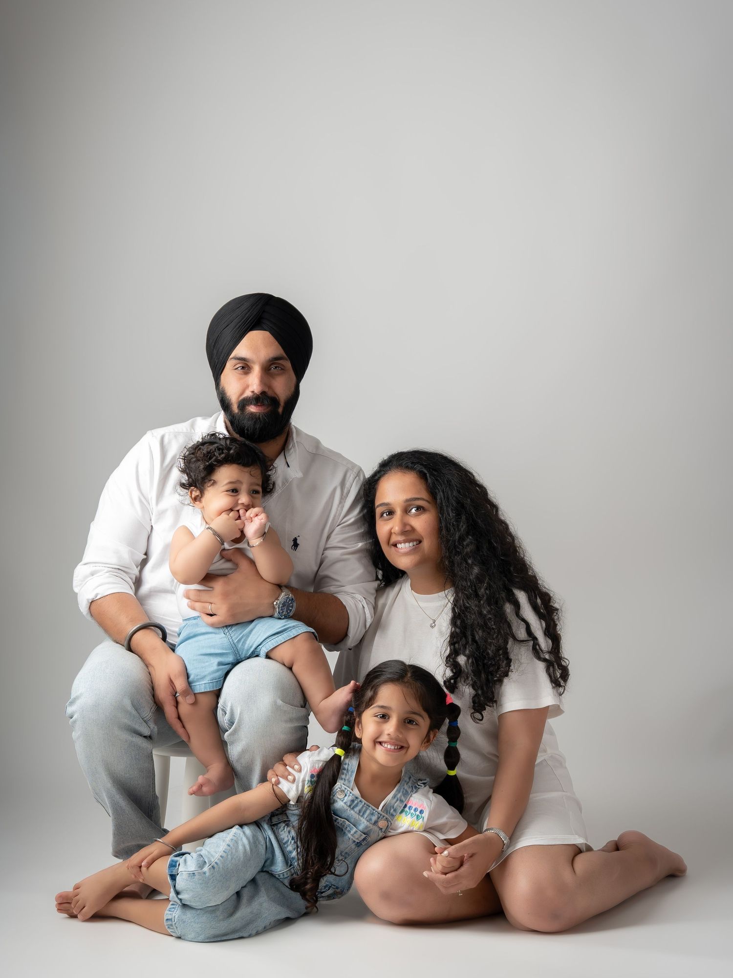 Sikh father in turban with family of four including baby and young daughter in studio.