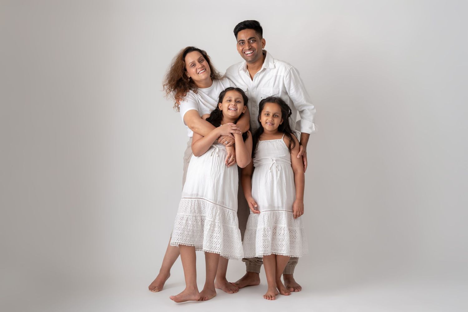Happy family of four in matching white outfits posing together in studio portrait.