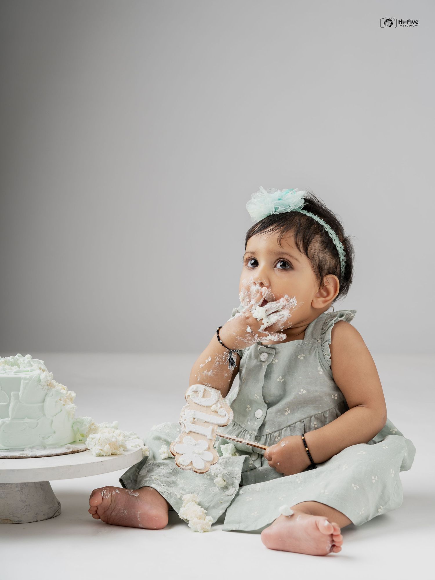 Baby girl eating birthday cake with frosting on face during fun first birthday cake smash photoshoot.