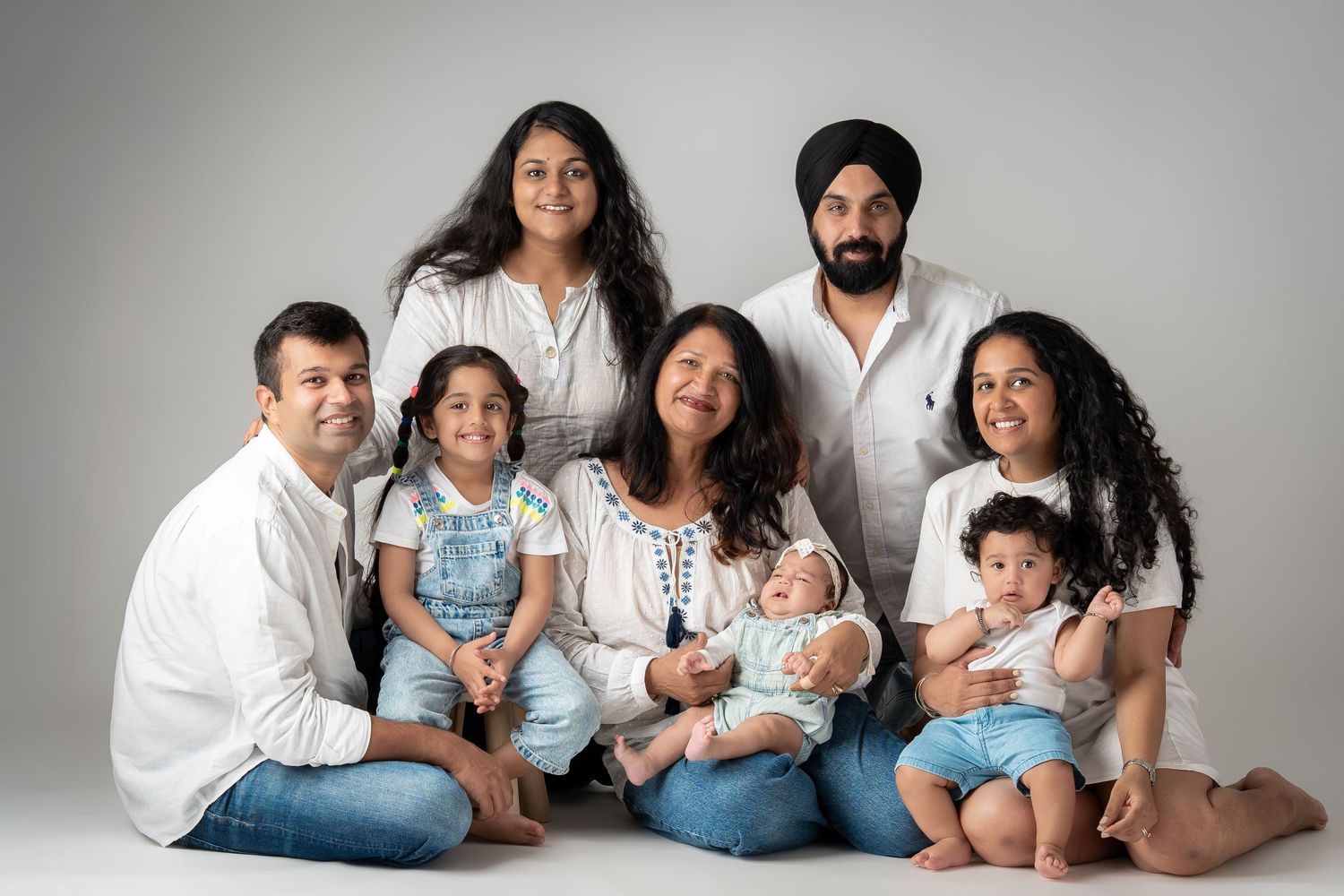 Large family group portrait with seven members in white and denim outfits in studio.