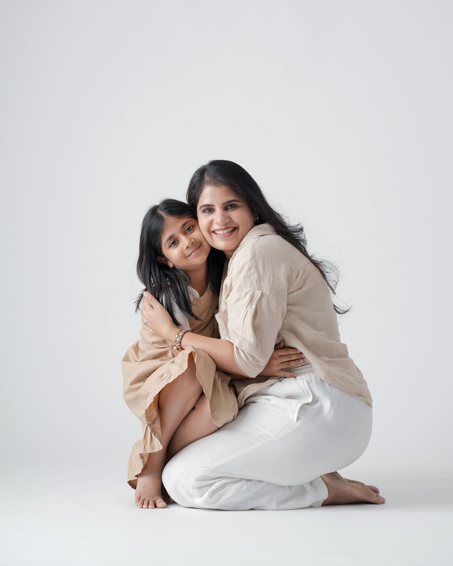 Mother and daughter hugging and smiling together in coordinating beige and white outfits.